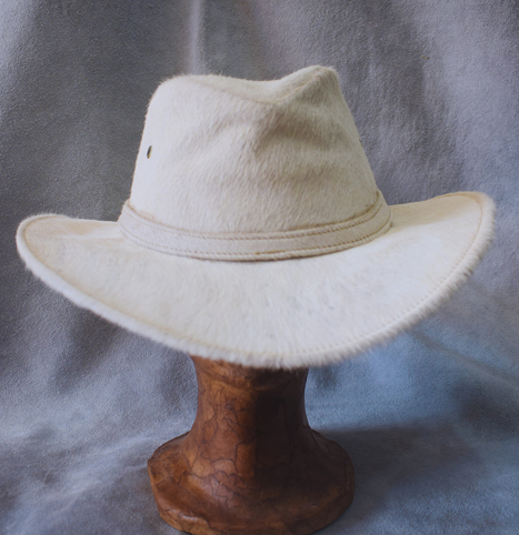 Sombrero de vaquero blanco sobre un soporte de madera sobre un fondo gris.