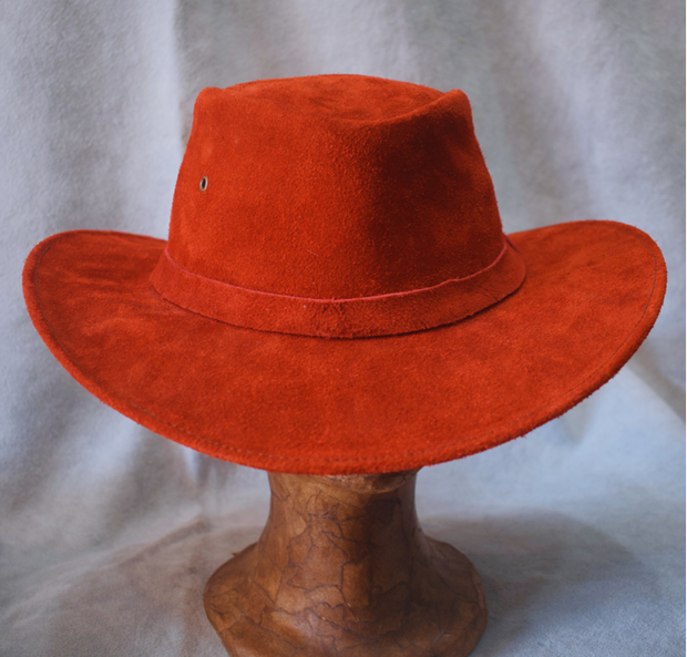 Sombrero de vaquero rojo de ala ancha sobre un soporte de madera contra un fondo gris.