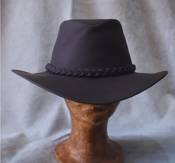 Sombrero de vaquero negro con banda trenzada sobre un soporte de madera contra un fondo gris.