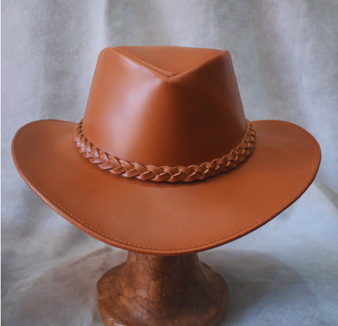Sombrero de vaquero de cuero marrón con banda trenzada sobre un soporte de madera.