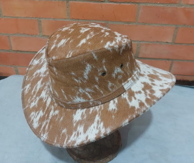 Sombrero de ala ancha con estampado marrón y blanco sobre un soporte contra una pared de ladrillos.