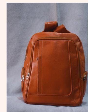 Mochila de cuero marrón con bolsillos delanteros con cremallera sobre fondo gris.