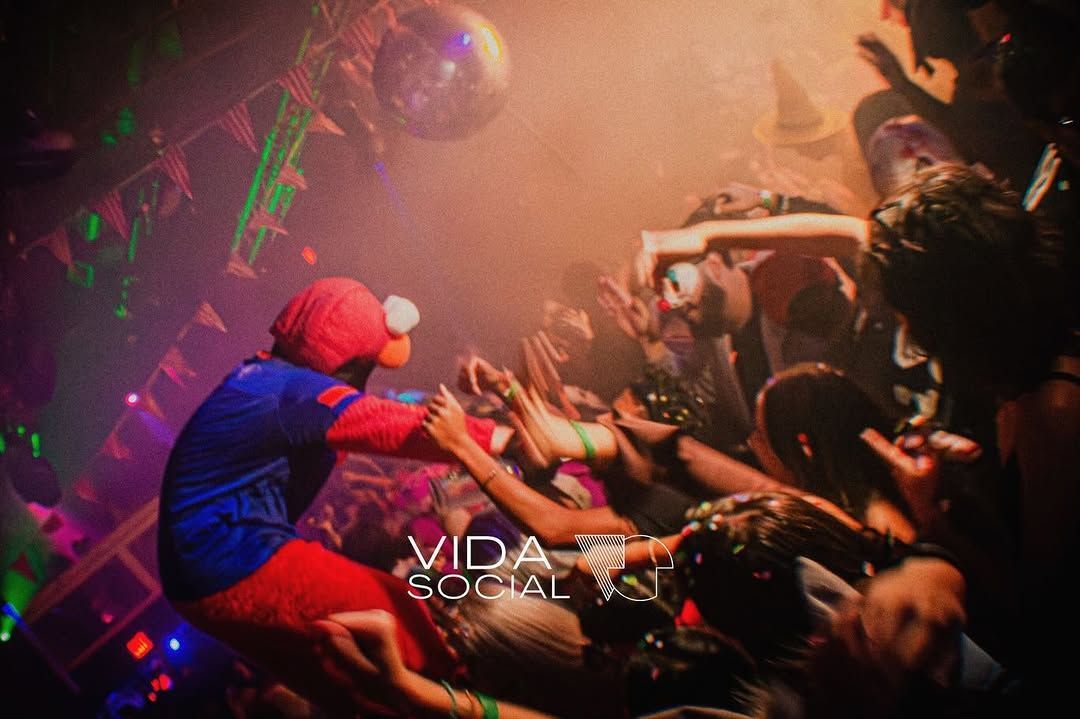 Person in red wig and blue outfit dancing in a crowded neon-lit nightclub