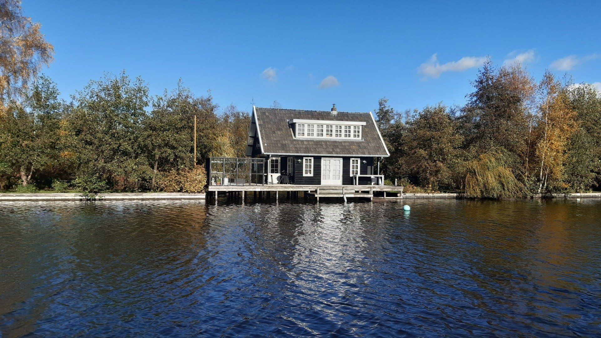 Zwarte hut op palen boven het water, omringd door bomen. Blauwe lucht.
