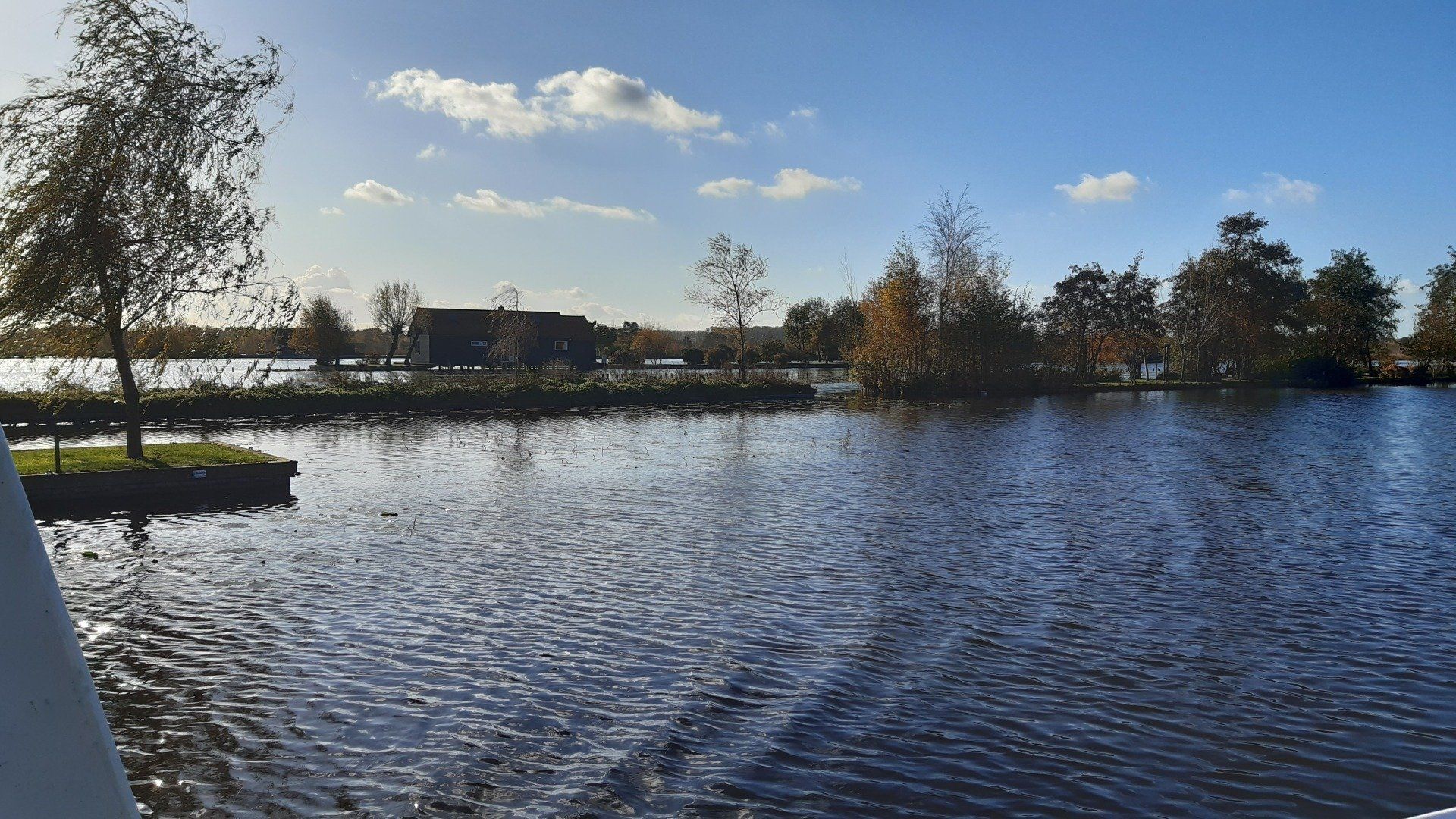 Een meer met kabbelend water, bomen op kleine eilandjes en een gebouw aan de horizon onder een zonnige blauwe hemel.