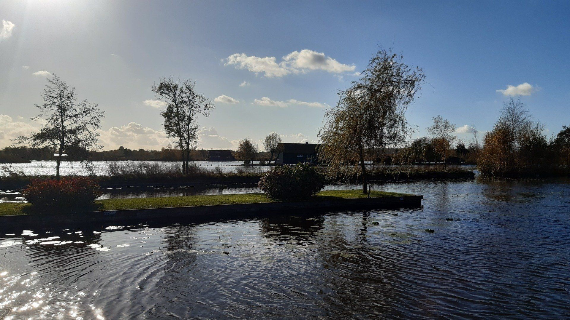 Uitzicht op het meer onder een stralende zon, met bomen op kleine eilandjes en een helderblauwe hemel.