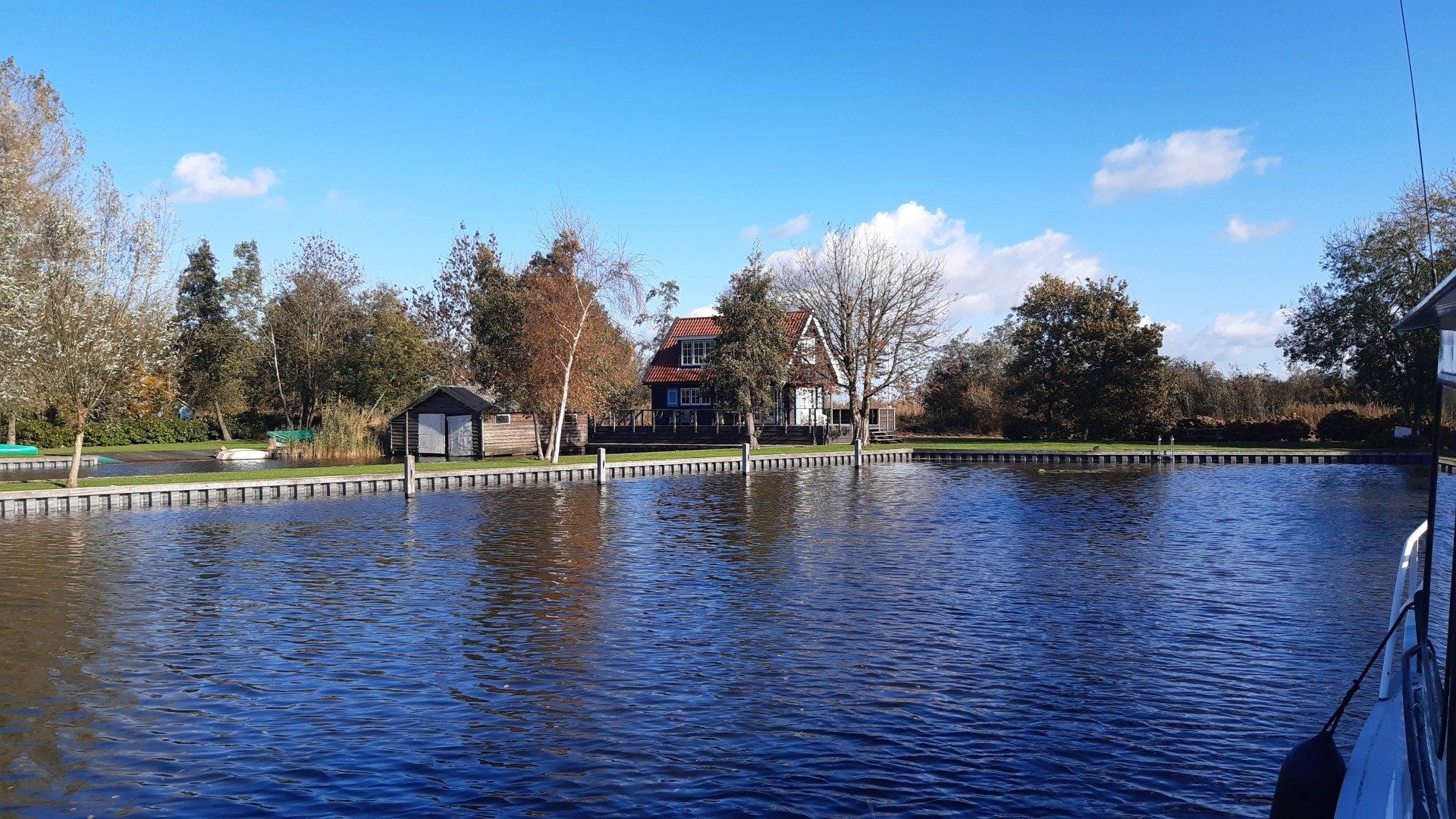 Rustig blauw water met bomen en een gebouw onder een helderblauwe hemel.