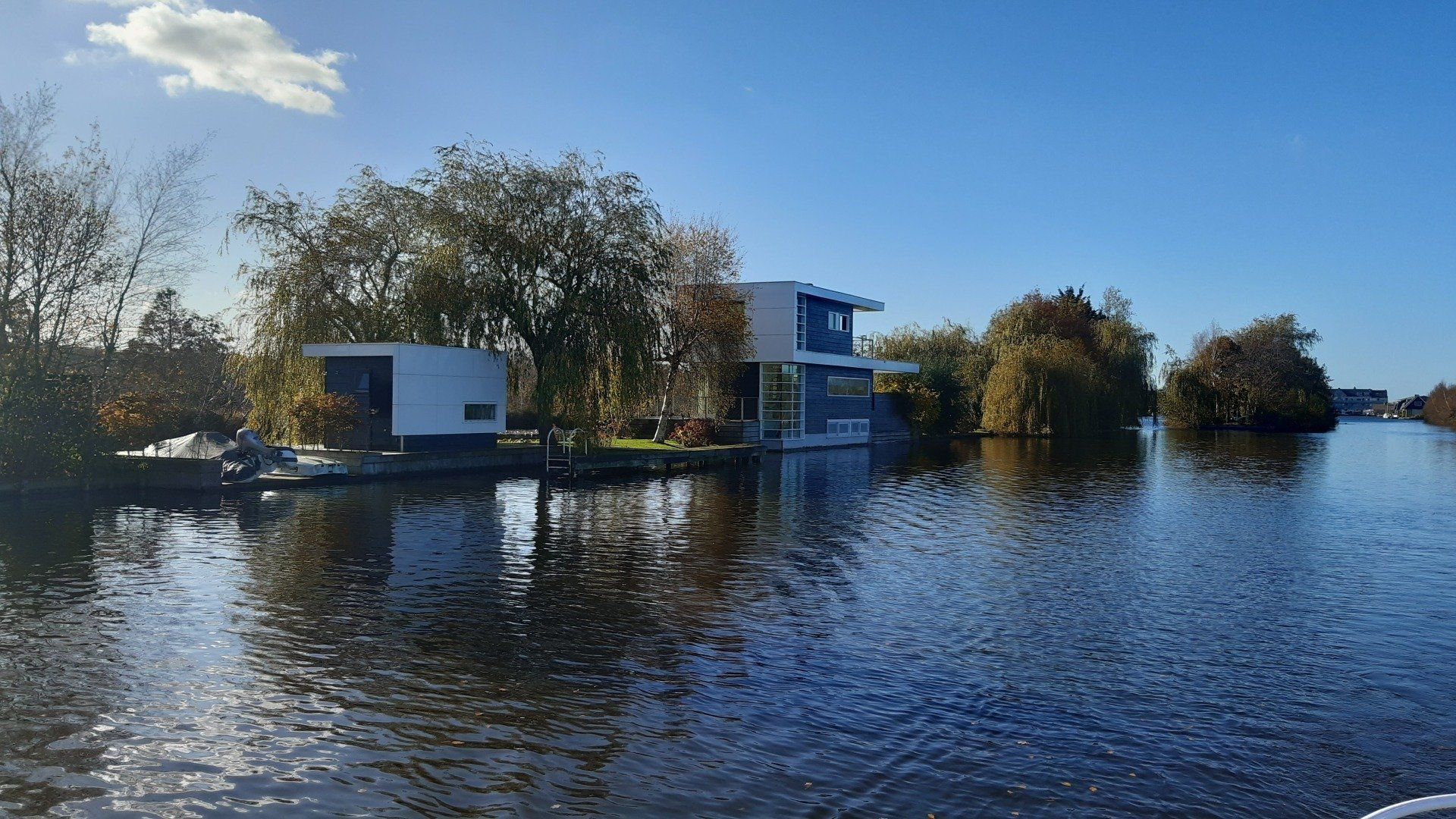 Moderne huizen aan het water, gelegen aan een kanaal met helder water, een blauwe lucht en bomen.