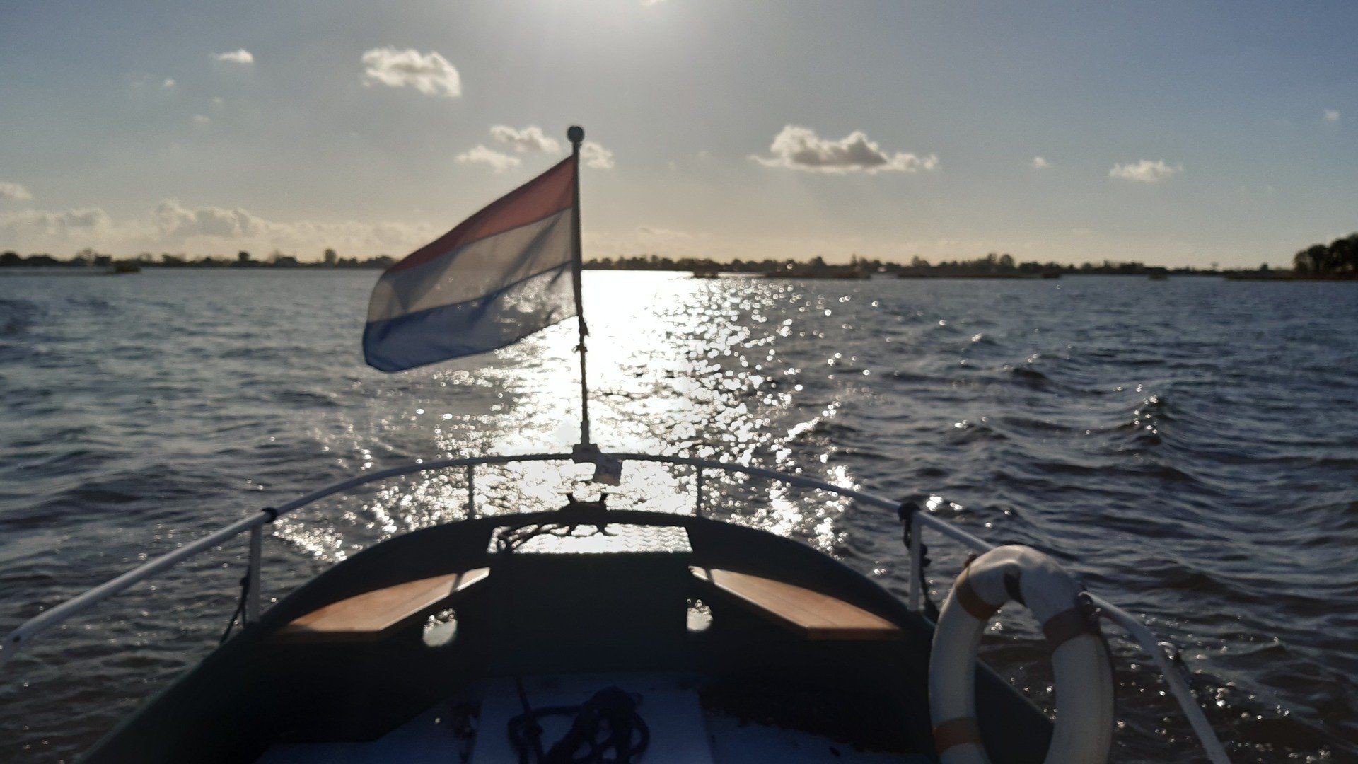 Boot op het water met Nederlandse vlag, zonlicht dat op de golven weerkaatst.