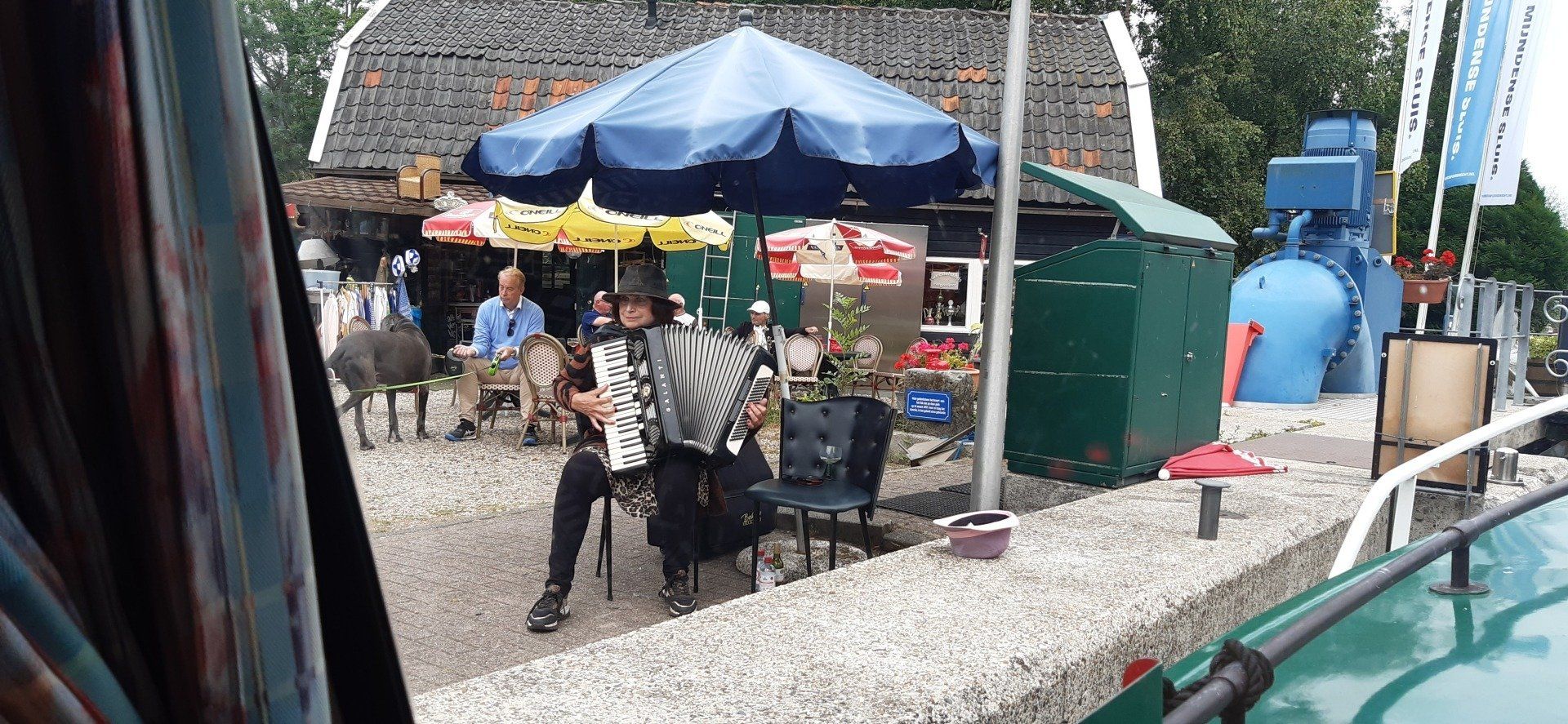 Anne van Egmond speelt accordeon onder een paraplu bij een gebouw. ​​Andere mensen zijn zichtbaar.
