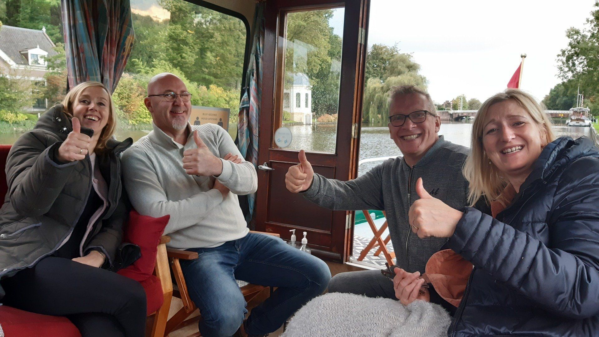 Vier mensen op een boot steken hun duim omhoog, met uitzicht op een rivier.