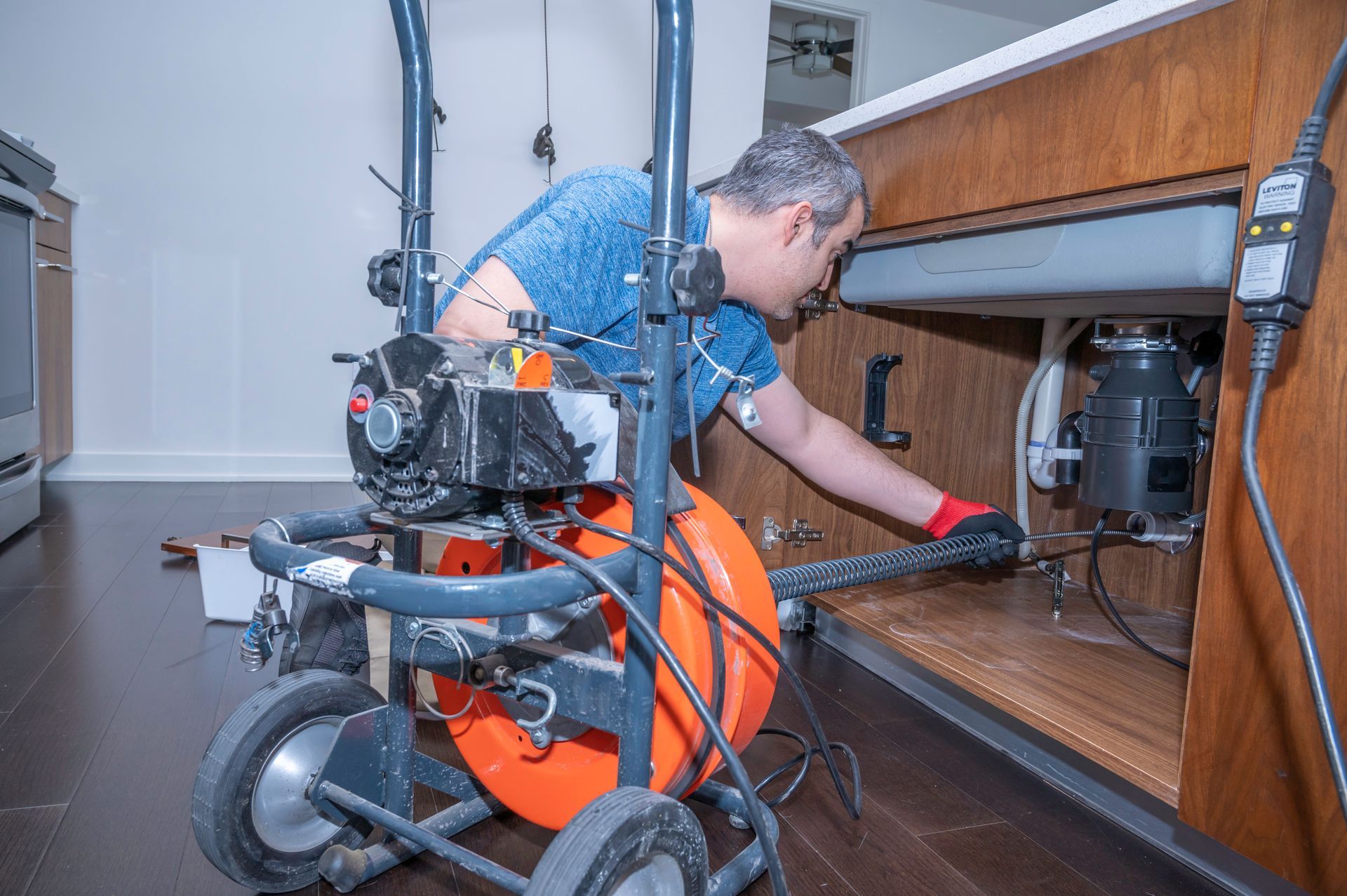 An experienced plumber using specialized equipment to clean kitchen sink pipes. An experienced plumber using specialized equipment to clean kitchen sink pipes.