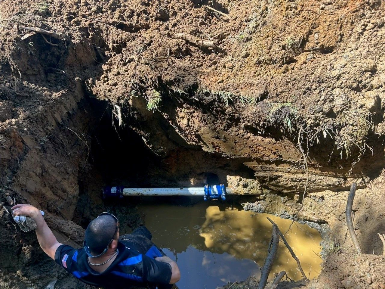 Person in blue gear enters a muddy cave pool with a flashlight in hand