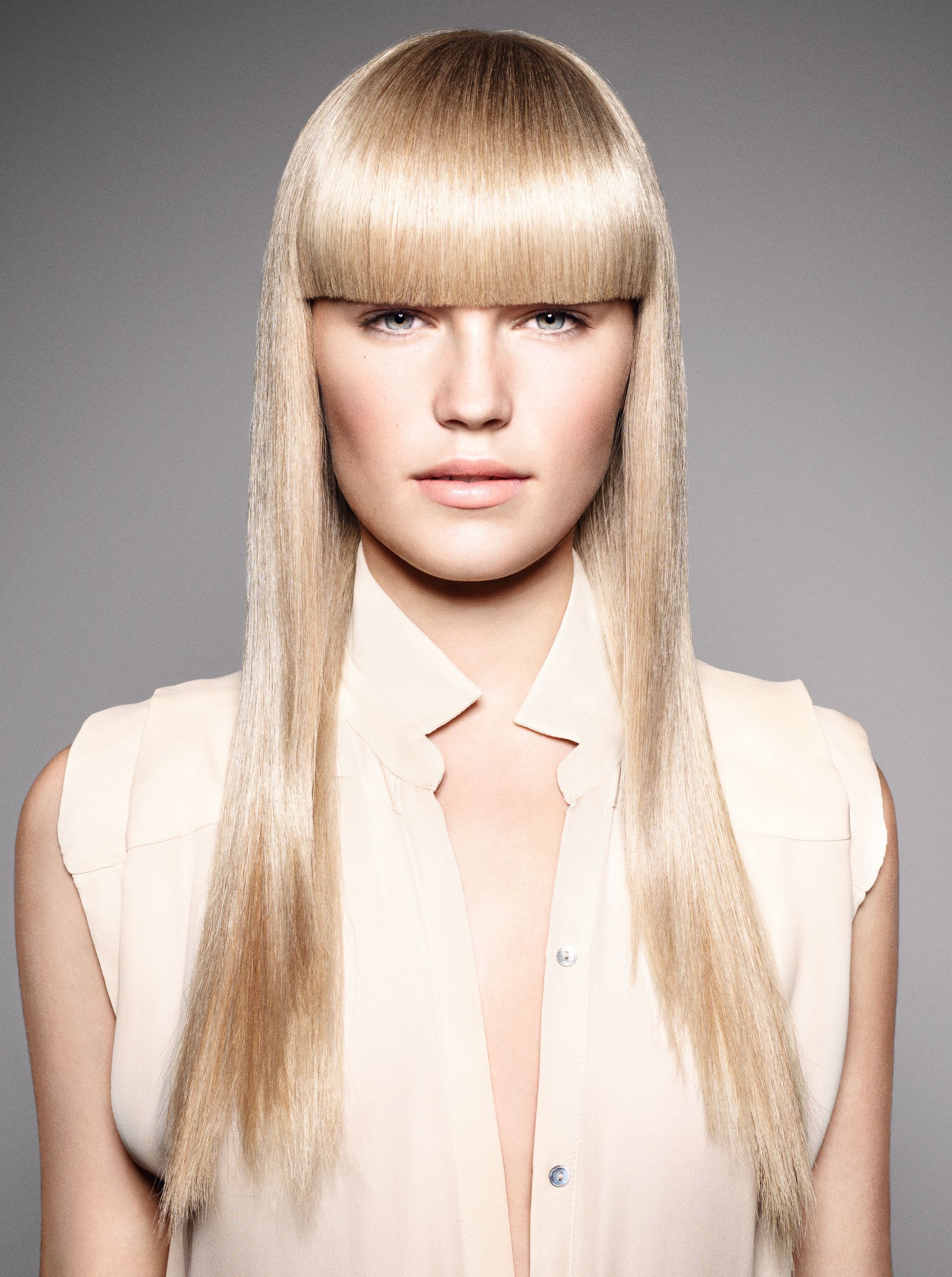 Woman with long, silver hair, dark blue roots, heavy eye makeup, and black, futuristic clothing against a dark background.