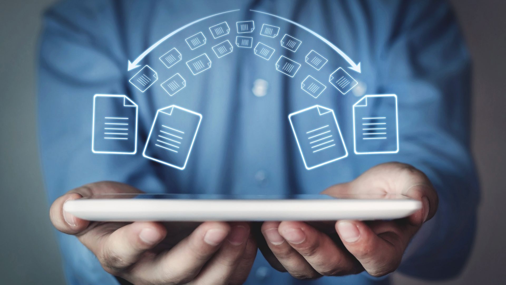 A man is holding a tablet with a bunch of files coming out of it