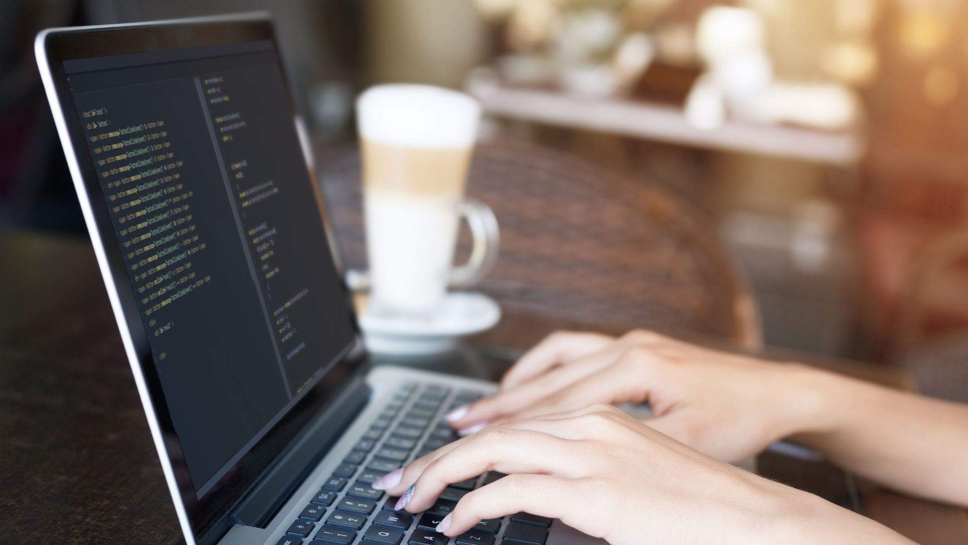 A person is typing on a laptop computer next to a cup of coffee.