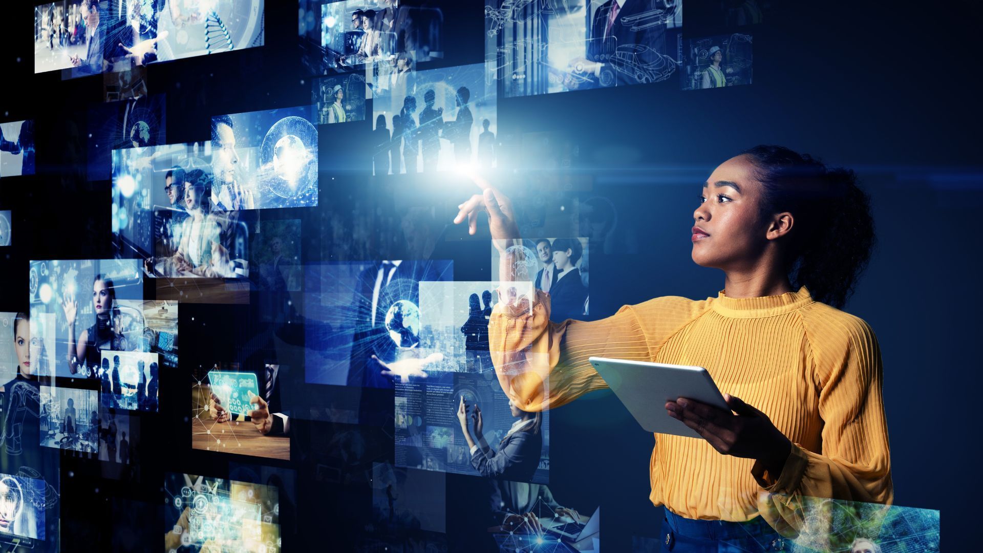 A woman is holding a tablet in front of a wall of pictures.