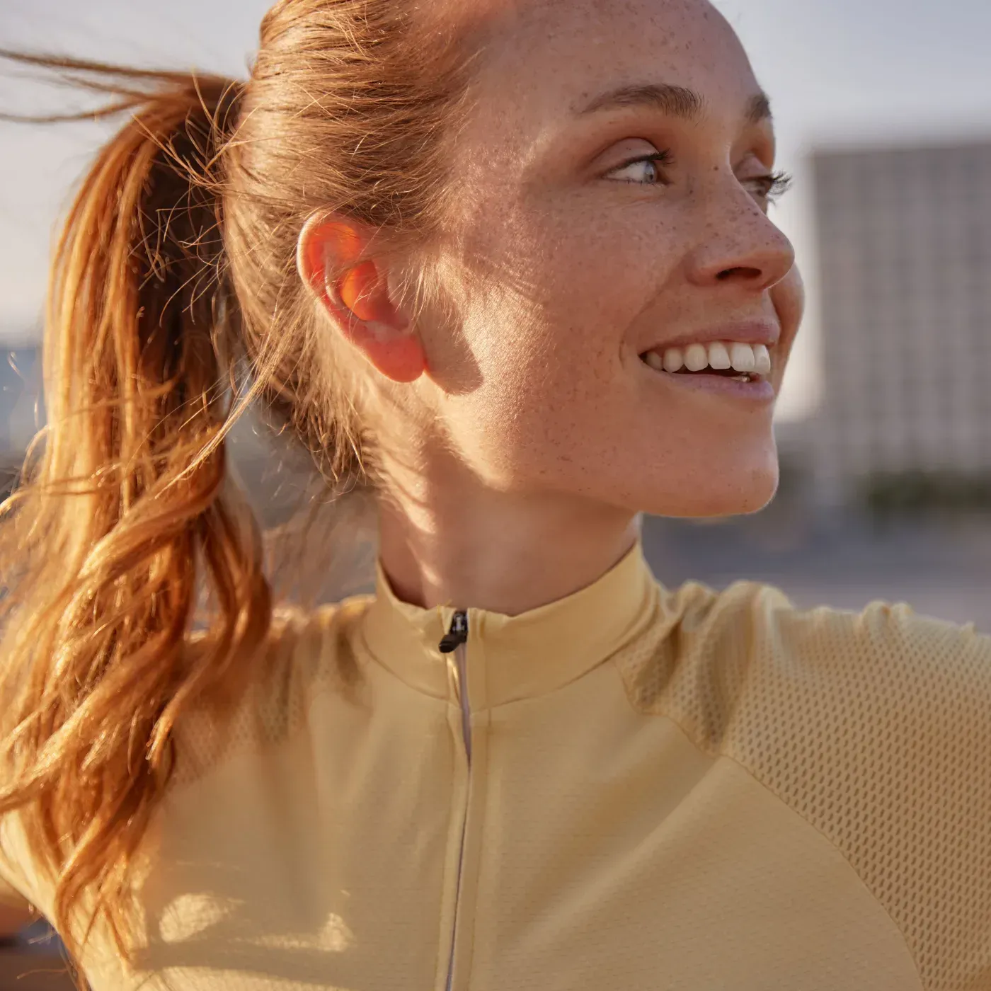 Woman in yellow athletic shirt smiles outdoors, hair in ponytail.