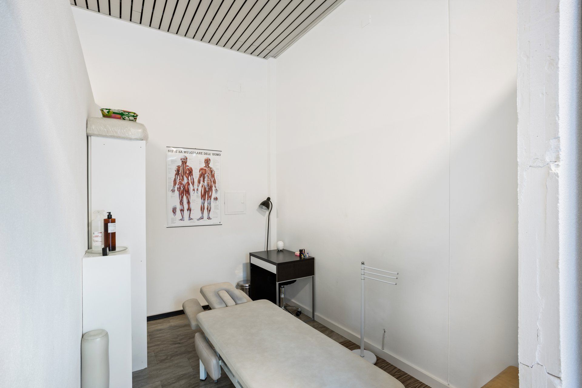Piccola sala medica con pareti bianche, dotata di tavolo per visite, cartella clinica, armadietto e lampada.