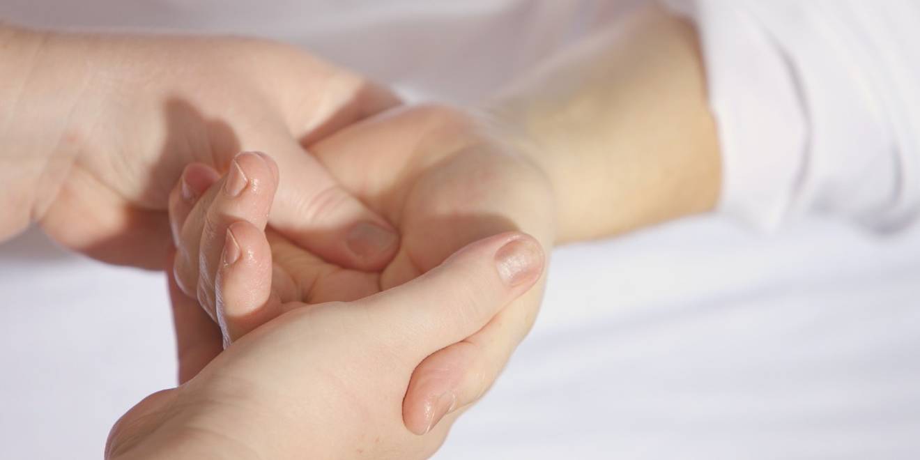 Due mani che tengono e massaggiano il polso di un'altra, probabilmente somministrando un trattamento medico o terapeutico.