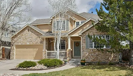 Suburban two-story stone house with beige siding, front porch, garage, and landscaped yard
