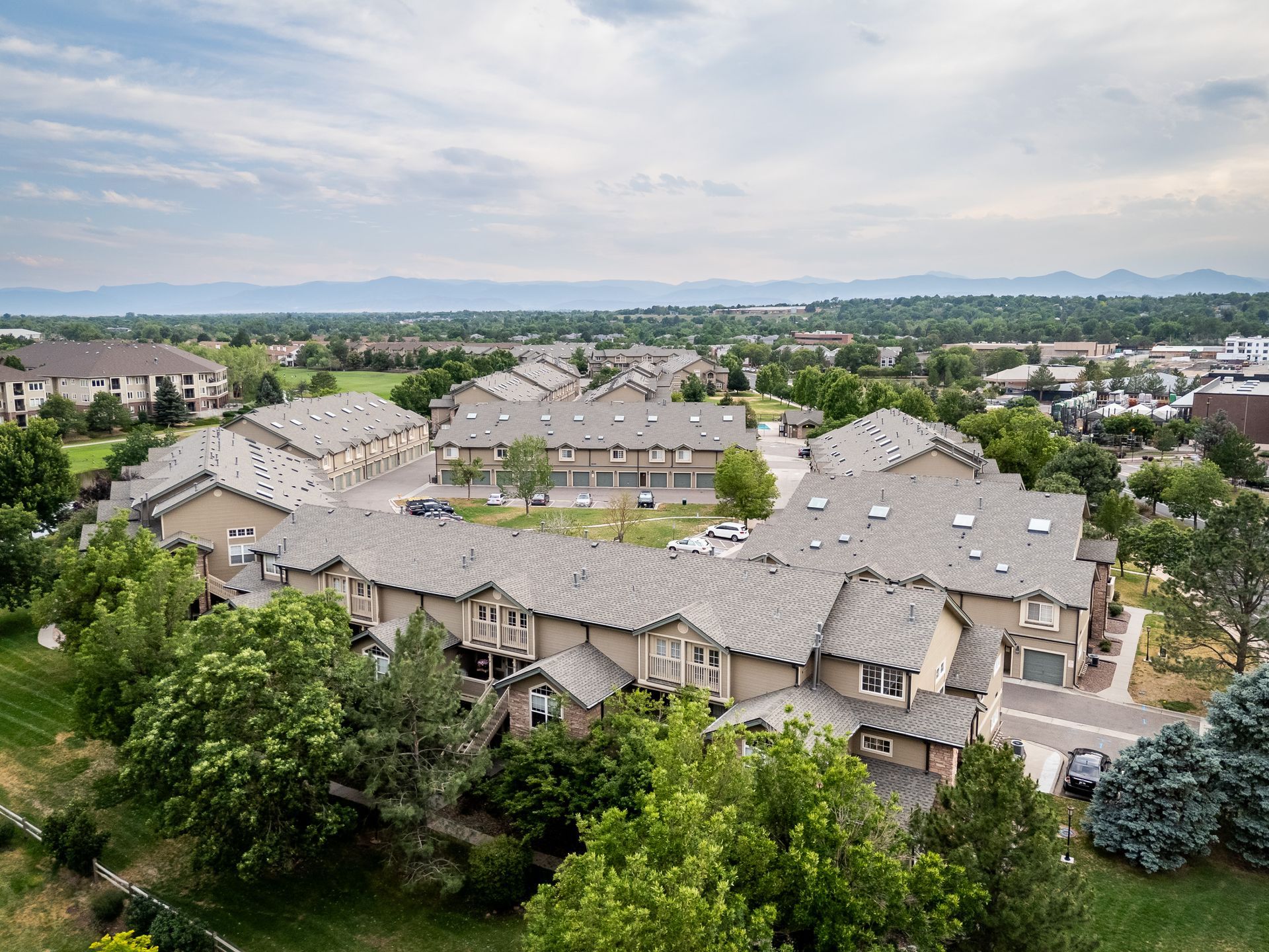 Aerial view of a suburban apartment complex with gray roofs, trees, and mountains in the distance