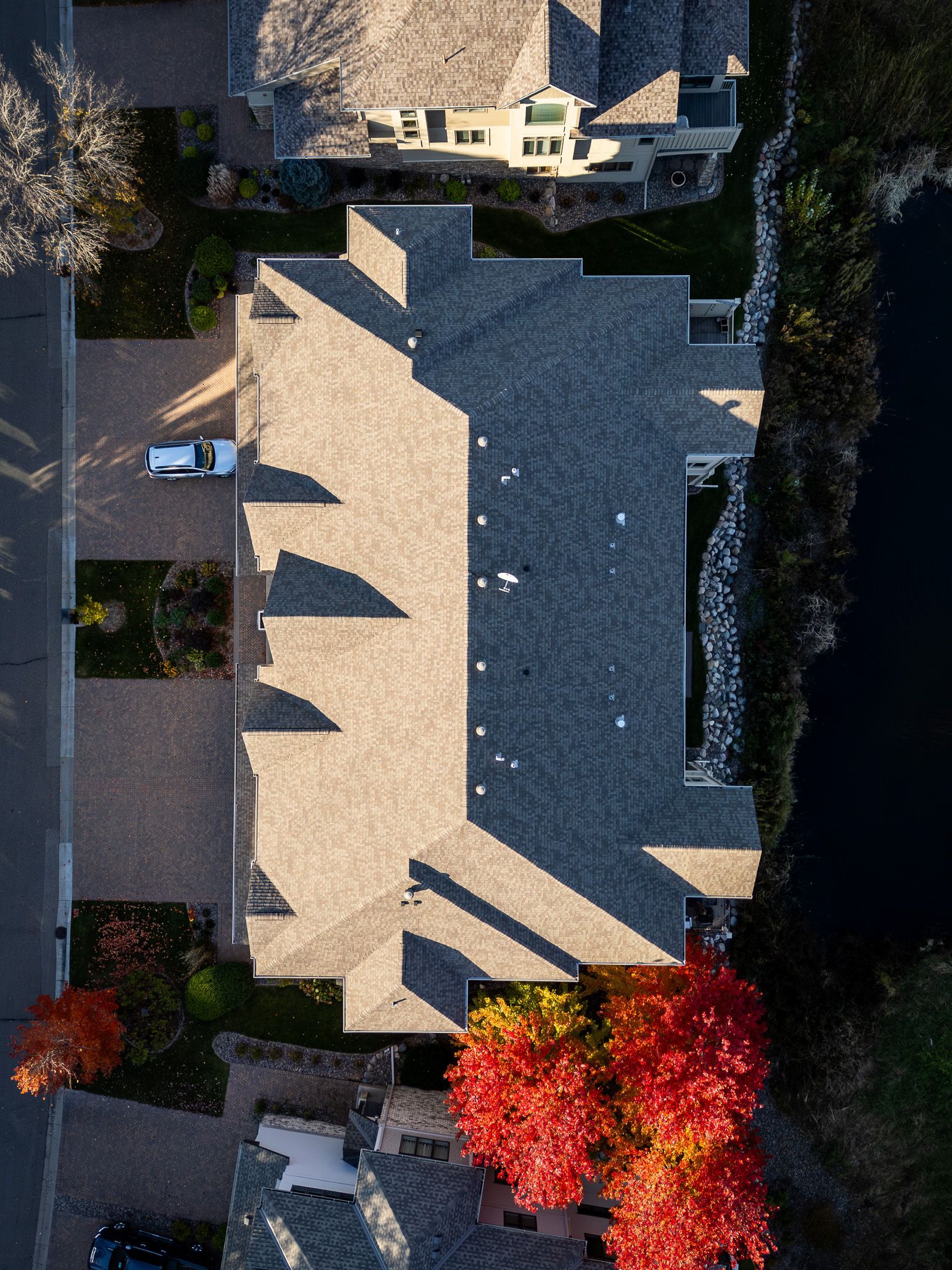 Aerial view of a house roof with bright red autumn trees and neighboring homes nearby