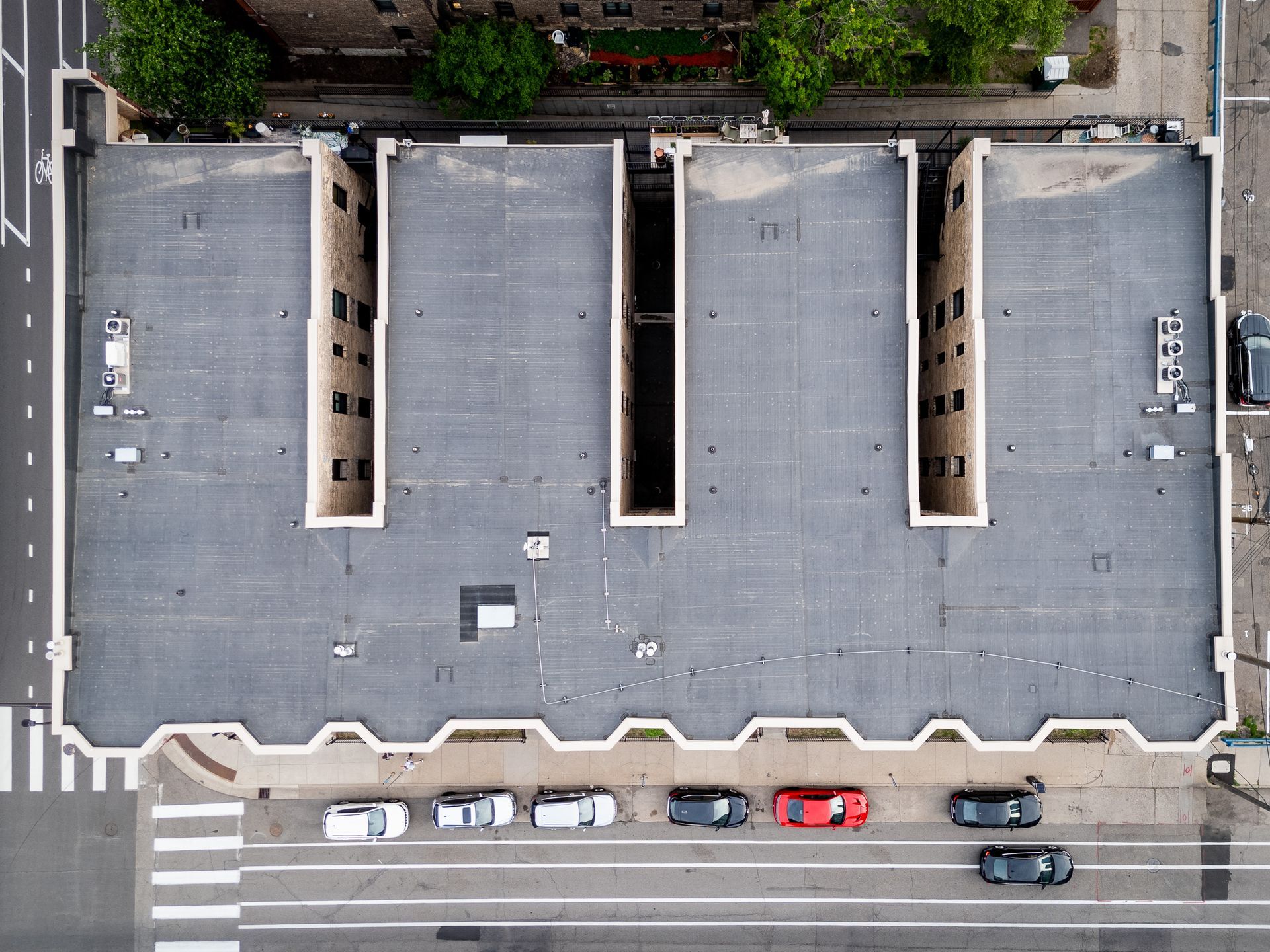 Aerial view of a flat-roofed building with skylights and parked cars along the street.