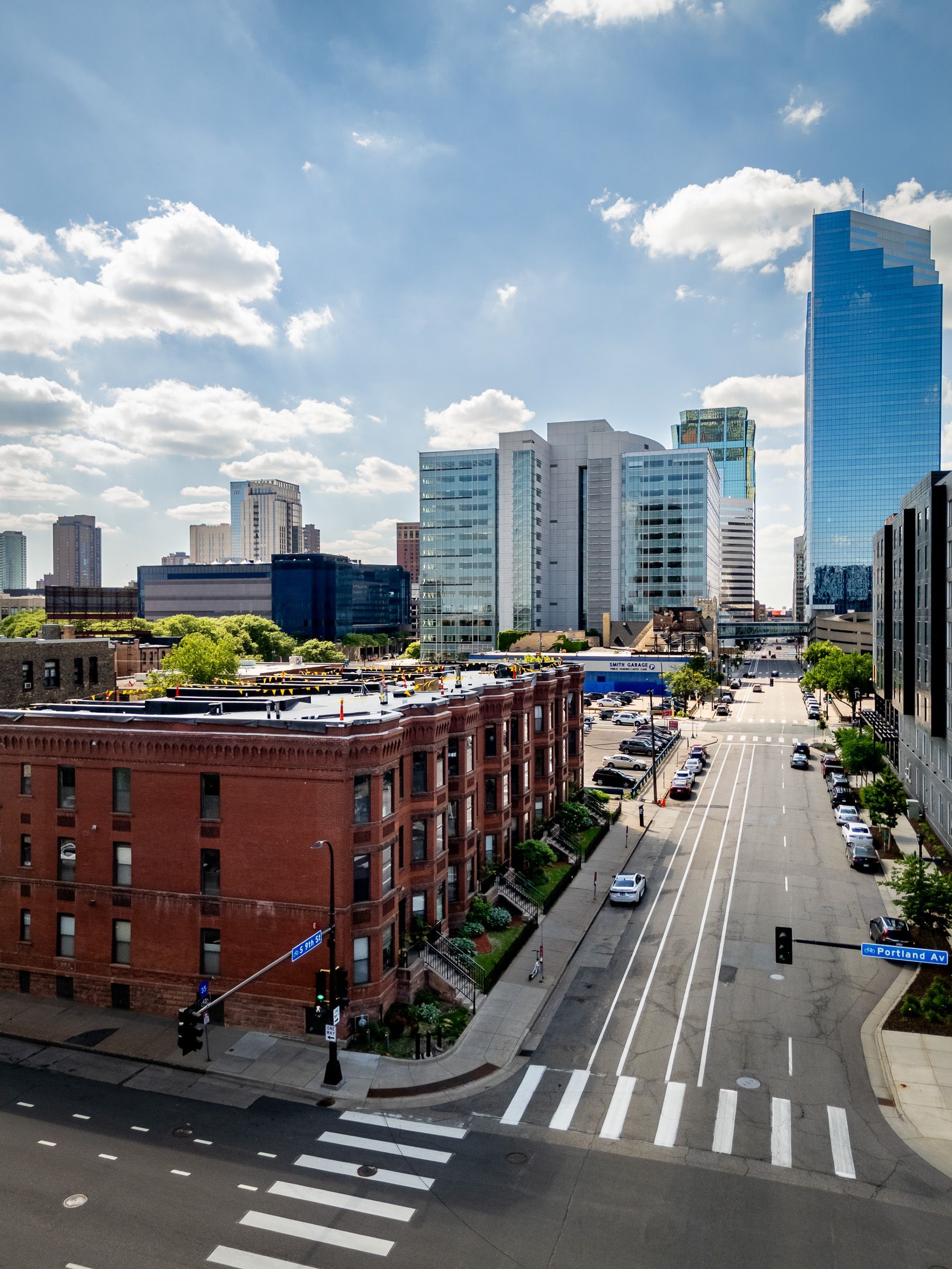 Downtown city street with red brick building, blue glass towers, and traffic under a cloudy sky