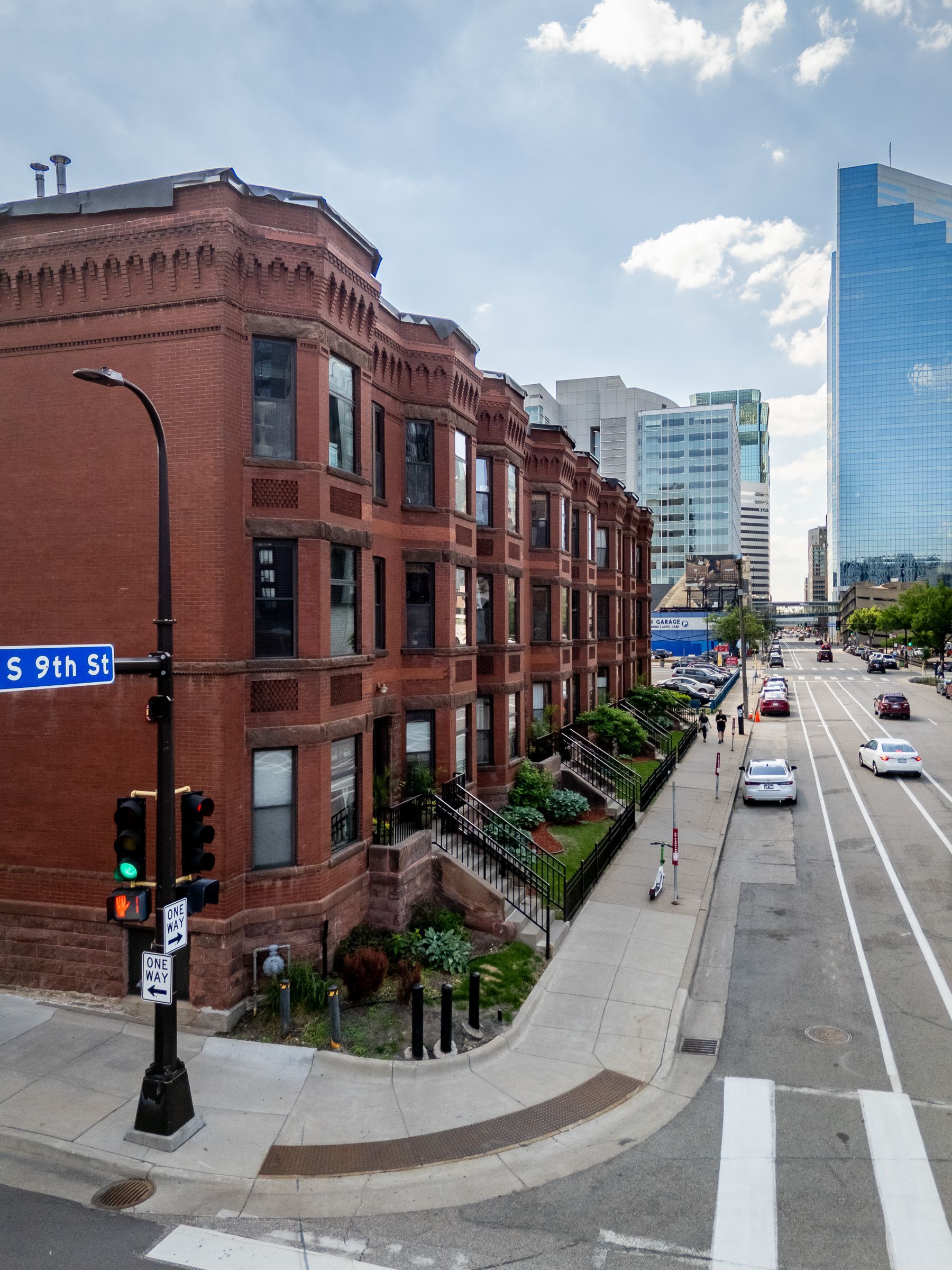 Brick rowhouses and a city street corner with traffic lights, a crosswalk, and tall modern buildings in the distance