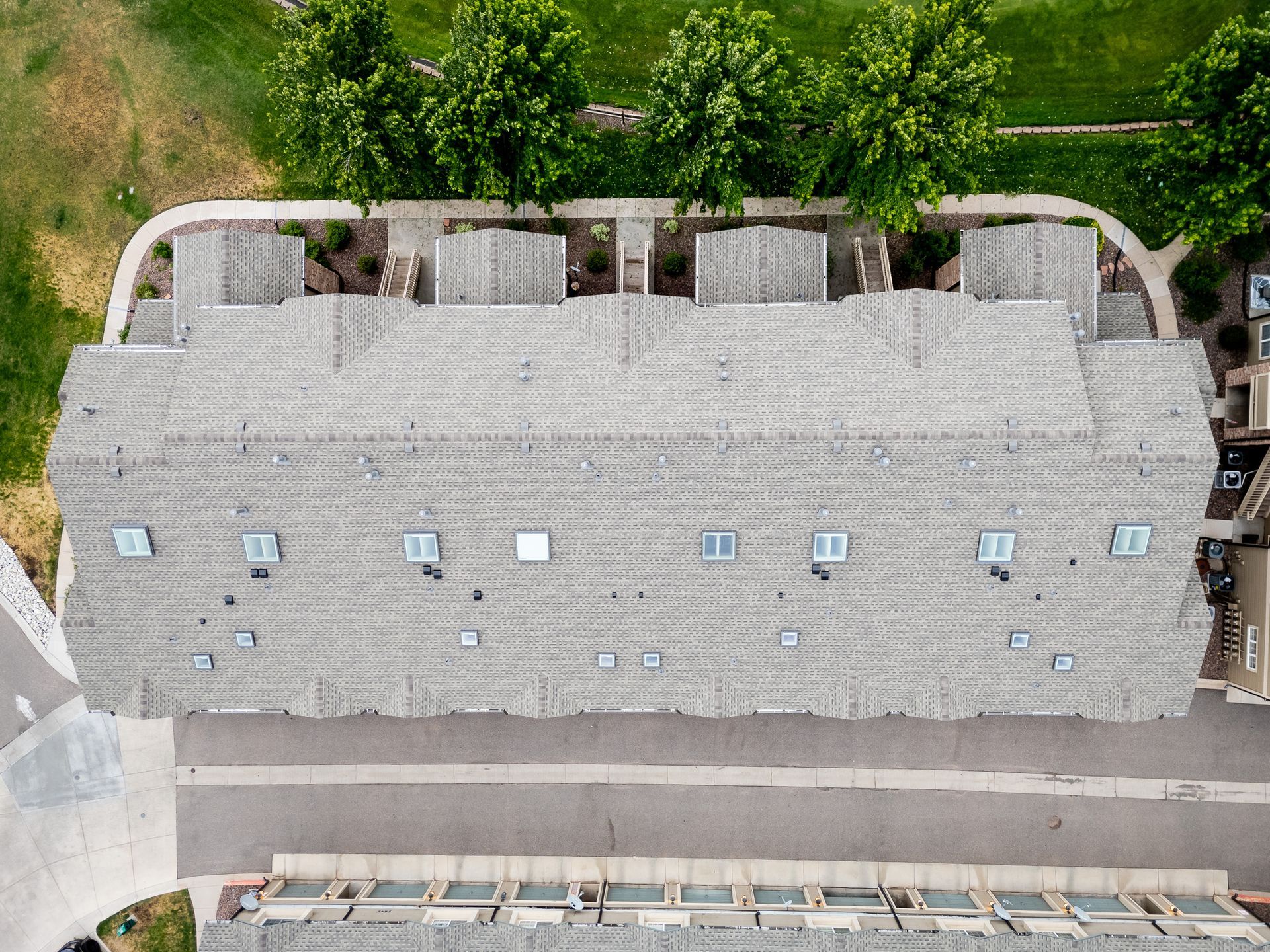 Aerial view of a large gray-roofed building beside a road and trees