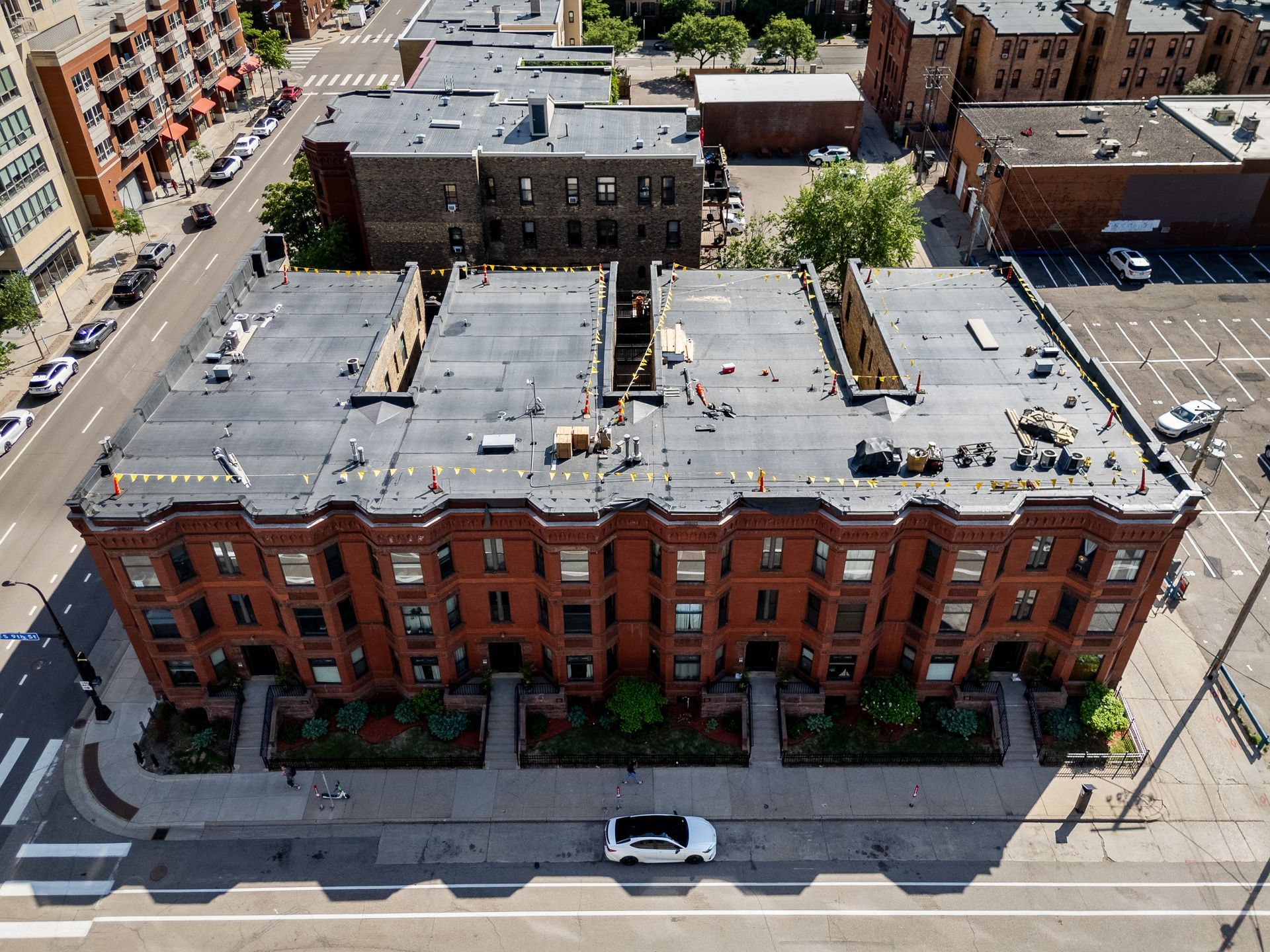 Aerial view of a red-brick apartment building on a city street with parked cars and nearby buildings.
