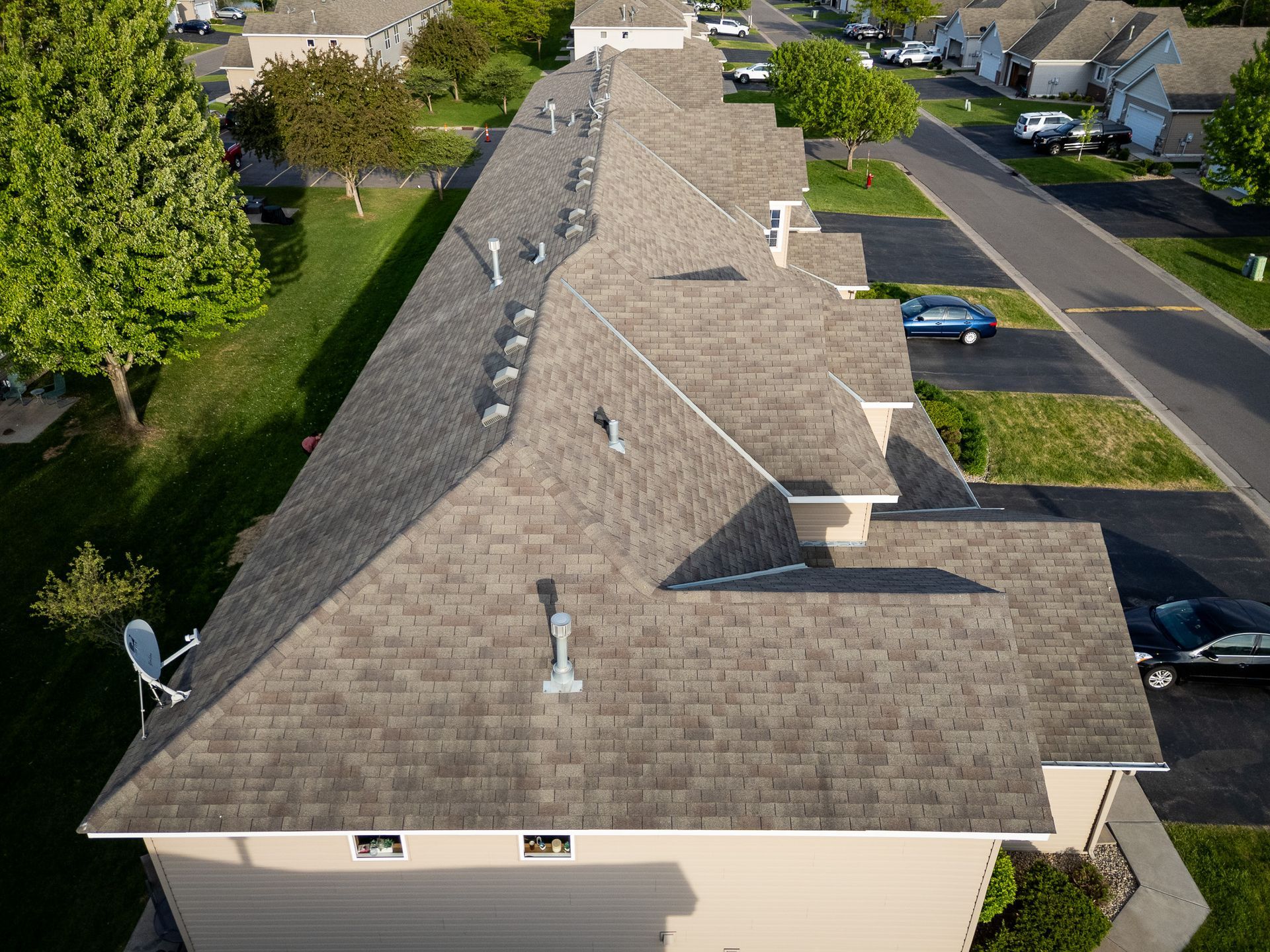 Aerial view of a suburban house roof with shingles, vents, and nearby street and trees