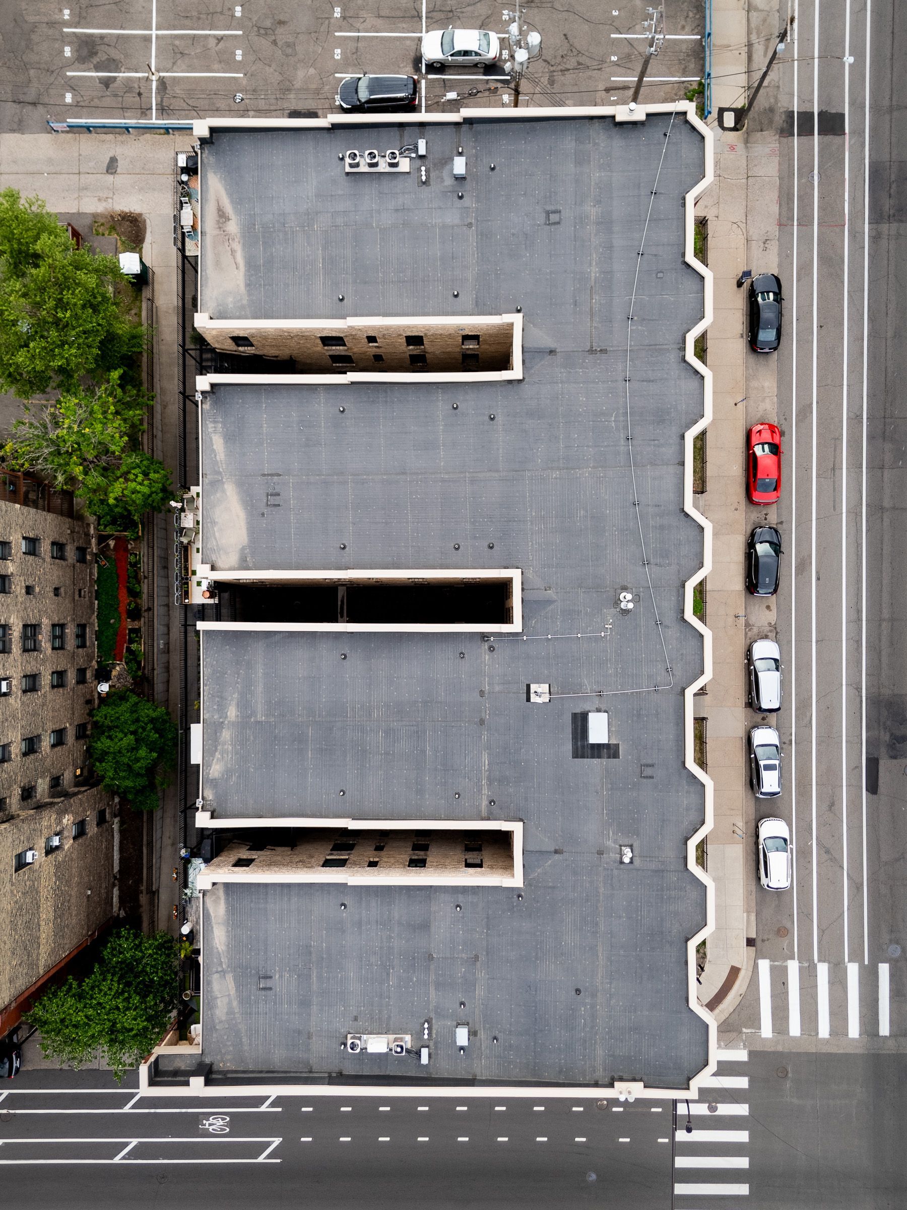 Aerial view of a flat-roofed building beside streets and parked cars at an intersection.