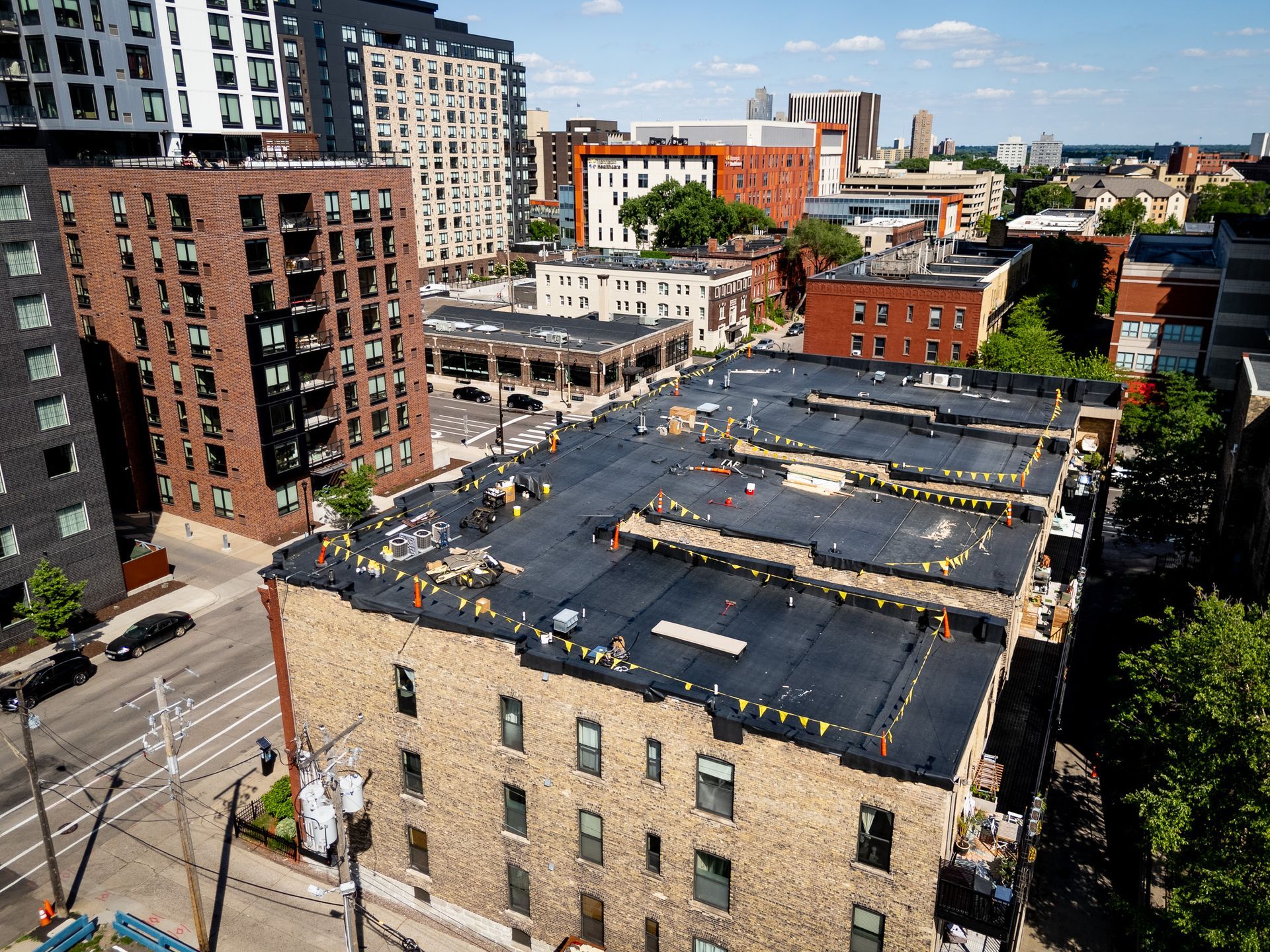 City rooftop with black roofing in an urban neighborhood, surrounded by brick buildings and streets.