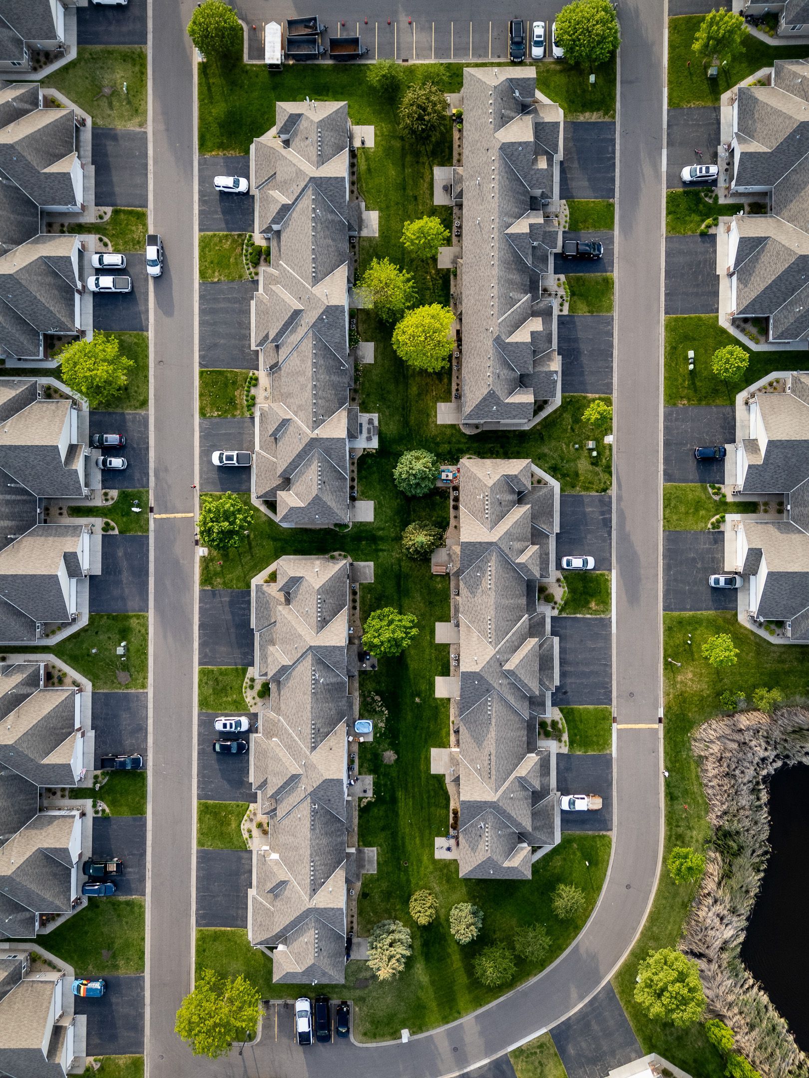 Aerial view of tan apartment buildings beside parking lots, roads, and green lawns with trees.