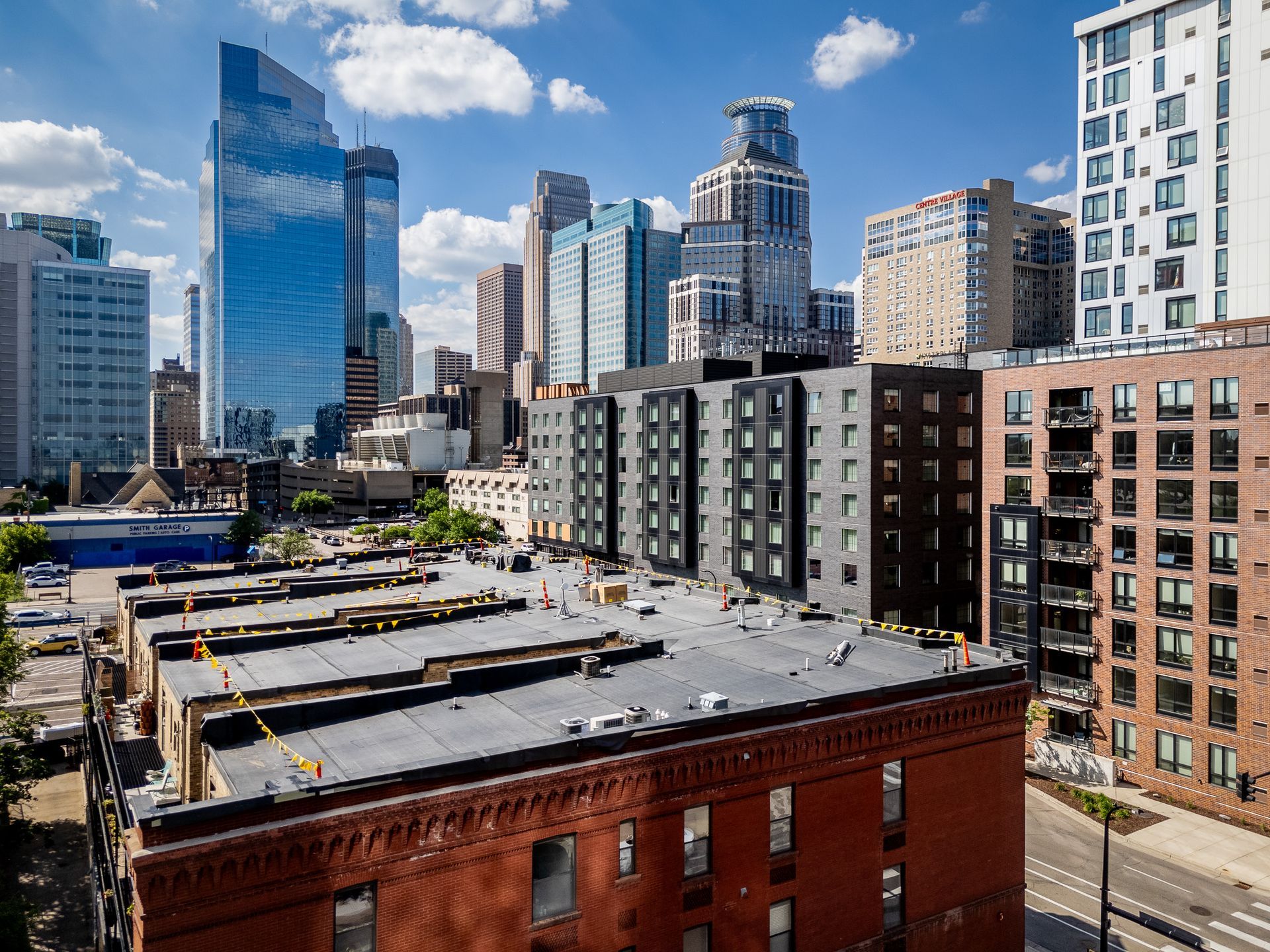 City skyline with modern high-rises above red brick buildings under a bright blue sky.