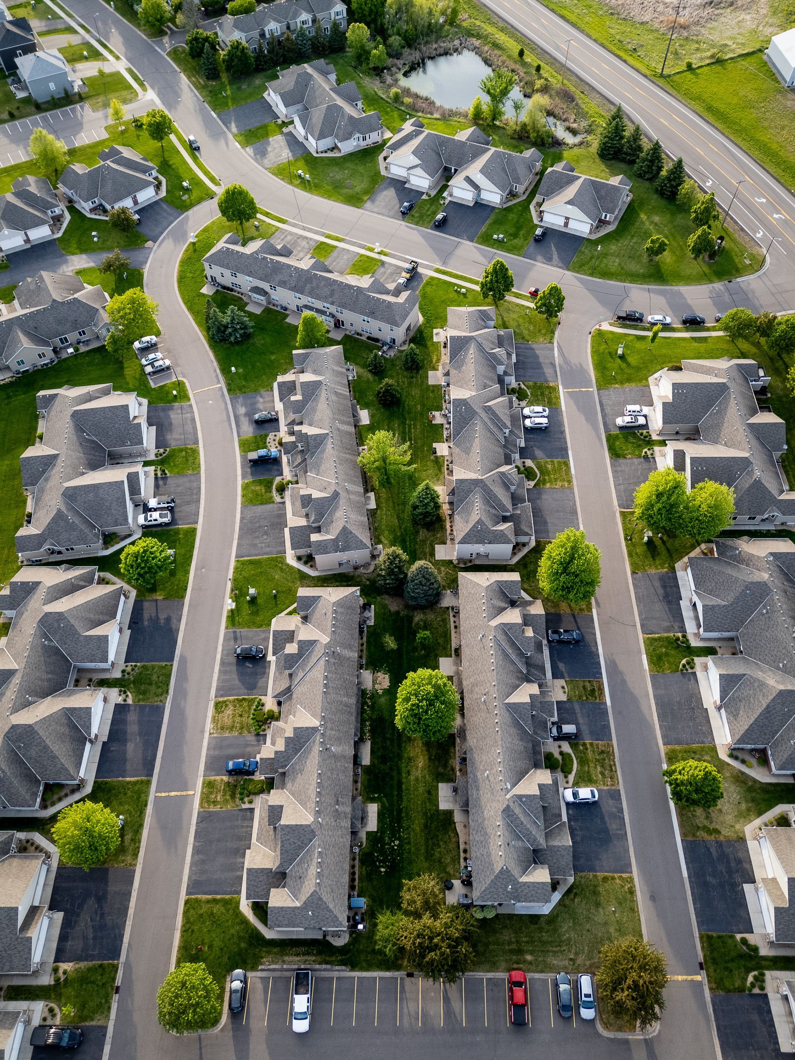 Aerial view of a suburban apartment complex with gray roofs, parked cars, and tree-lined streets.