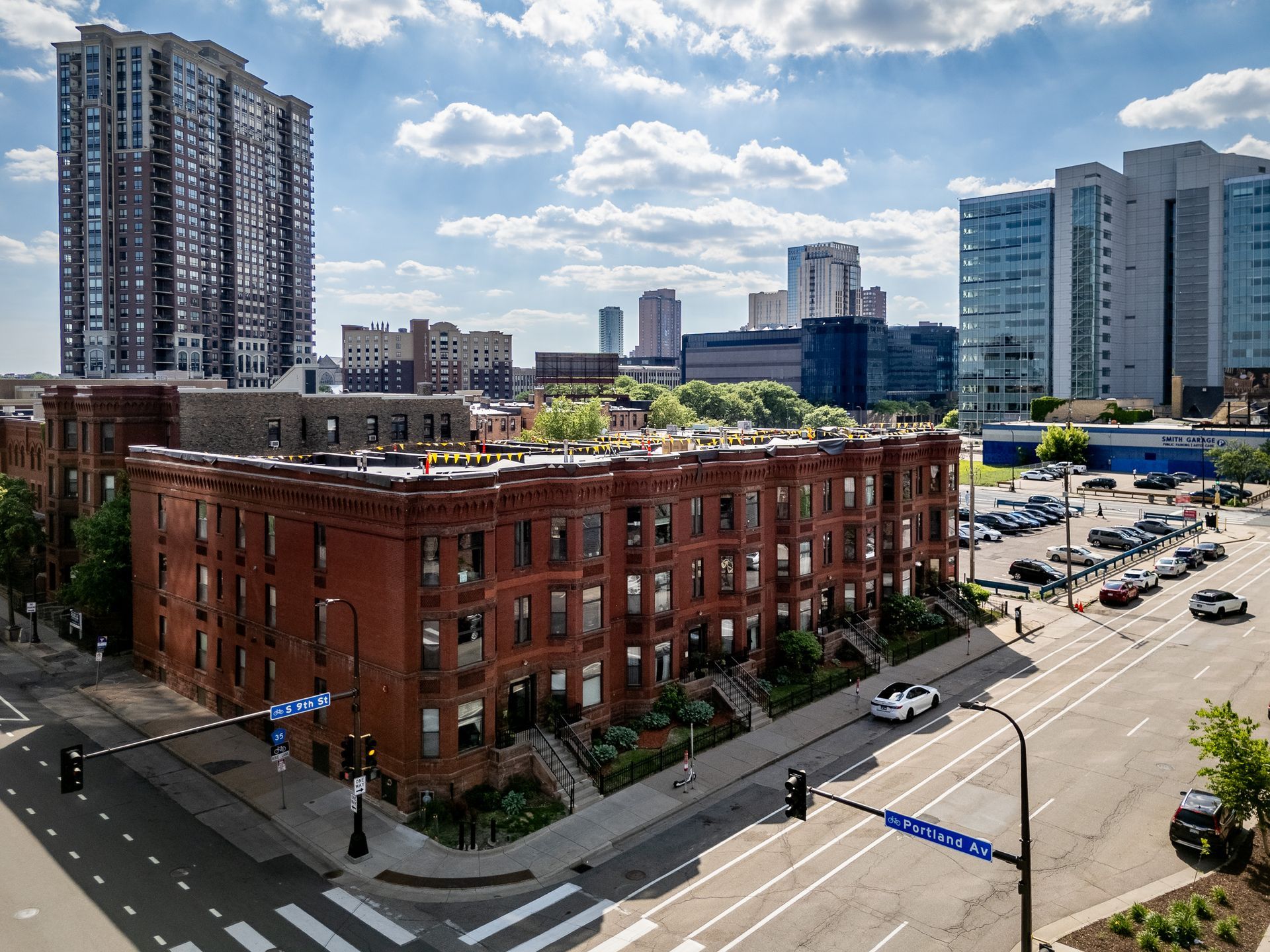 Red brick building at a city intersection, surrounded by modern high-rises under a partly cloudy sky