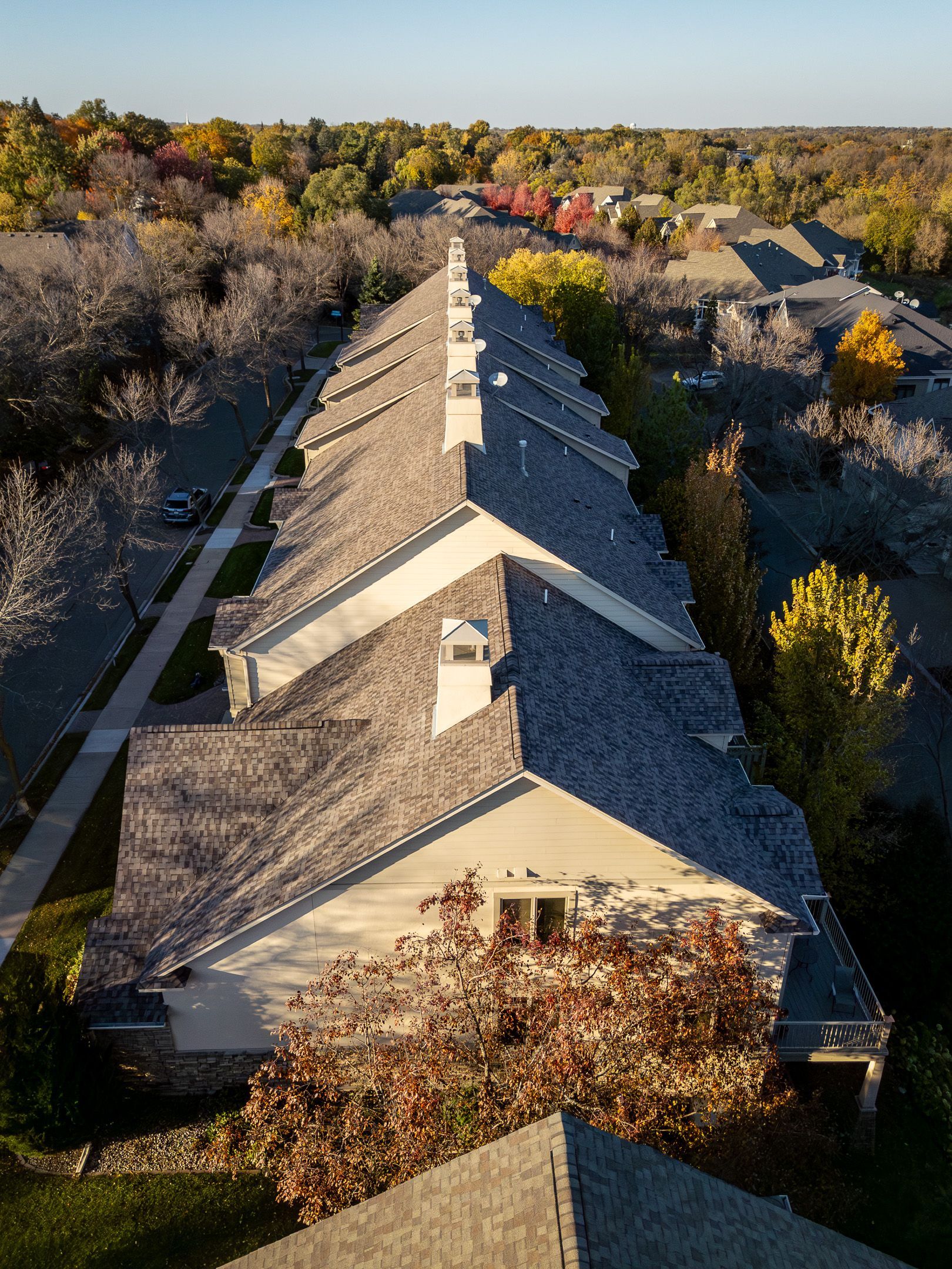 Aerial view of a long beige apartment building with a gray roof surrounded by autumn trees.