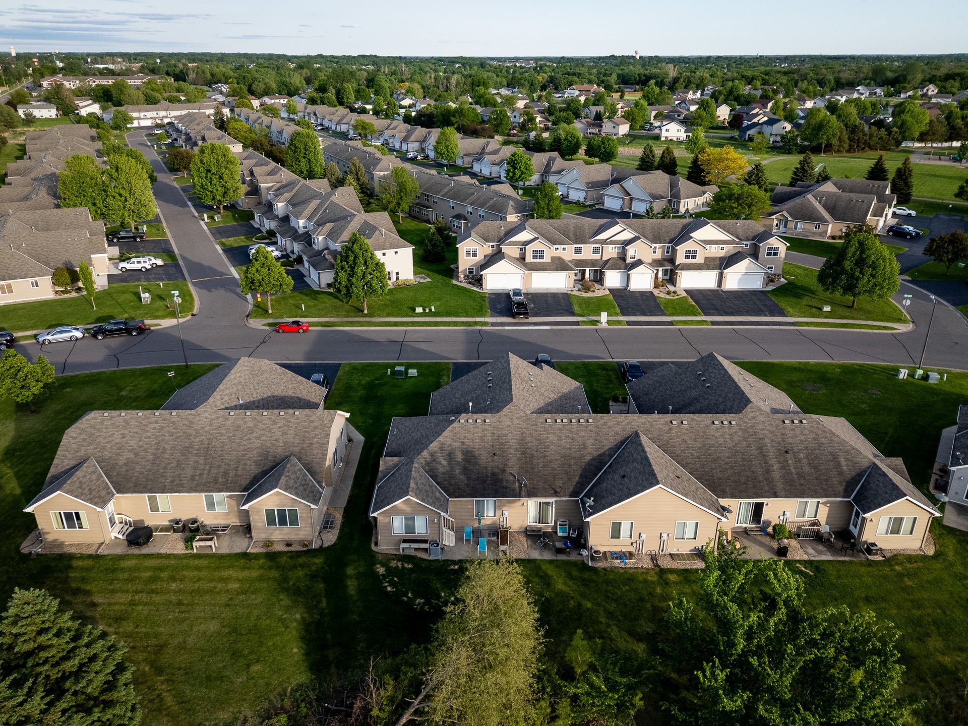 Aerial view of a suburban neighborhood with rows of houses, streets, and green lawns under clear daylight