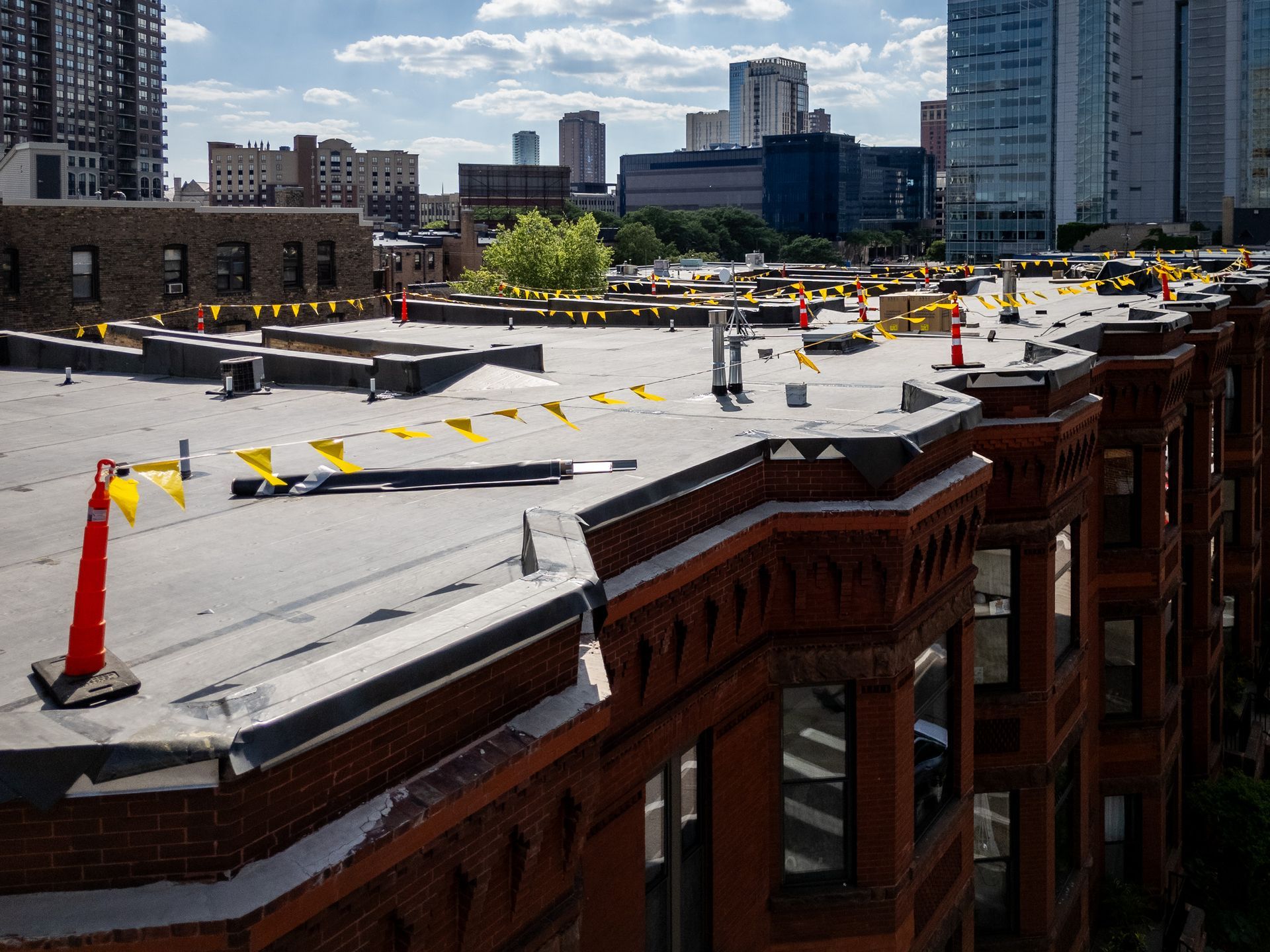 Rooftop construction site atop a brick building, with safety cones and city skyline in the background.