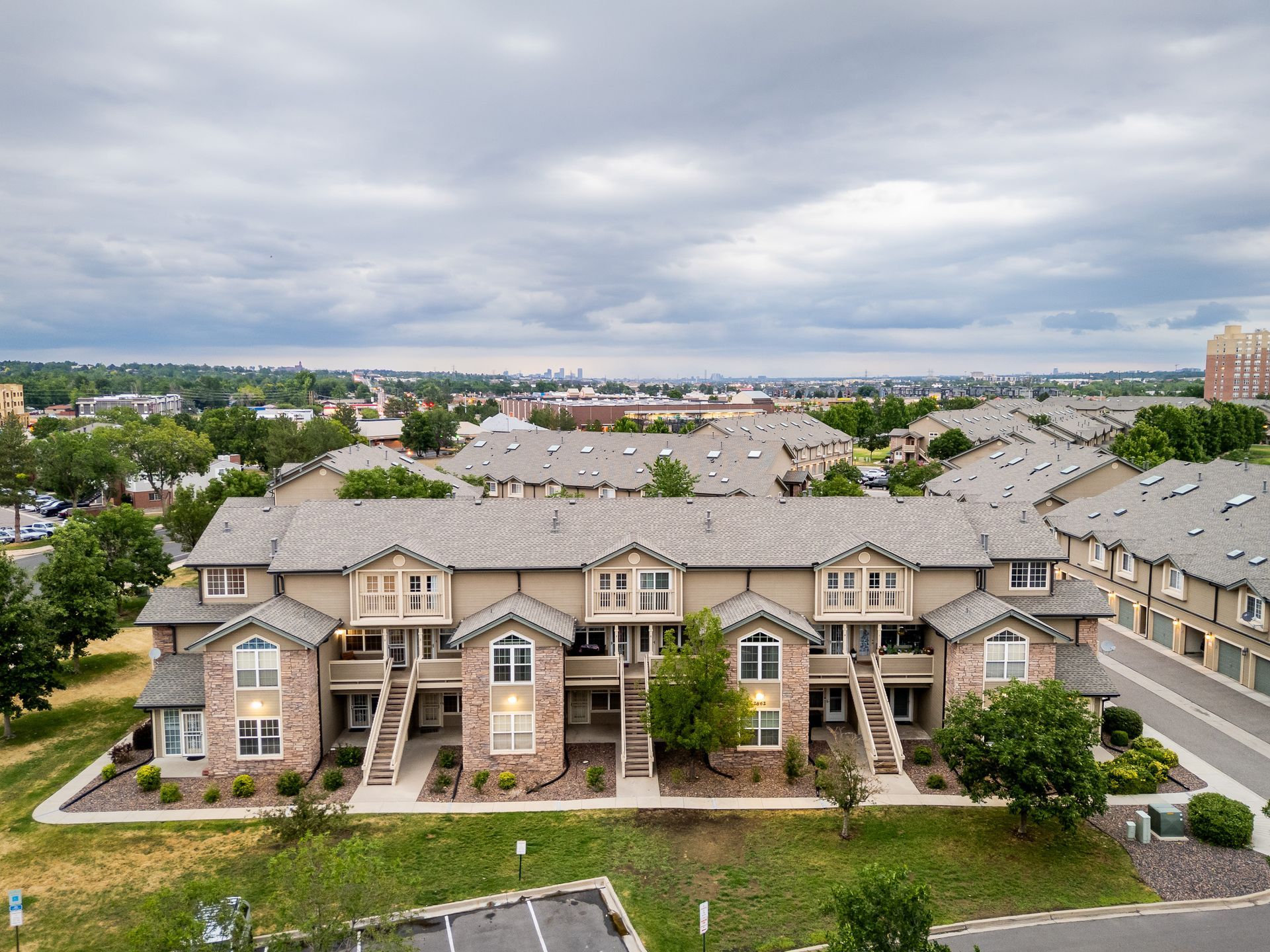 Aerial view of tan apartment buildings with gray roofs under a cloudy sky in a suburban complex