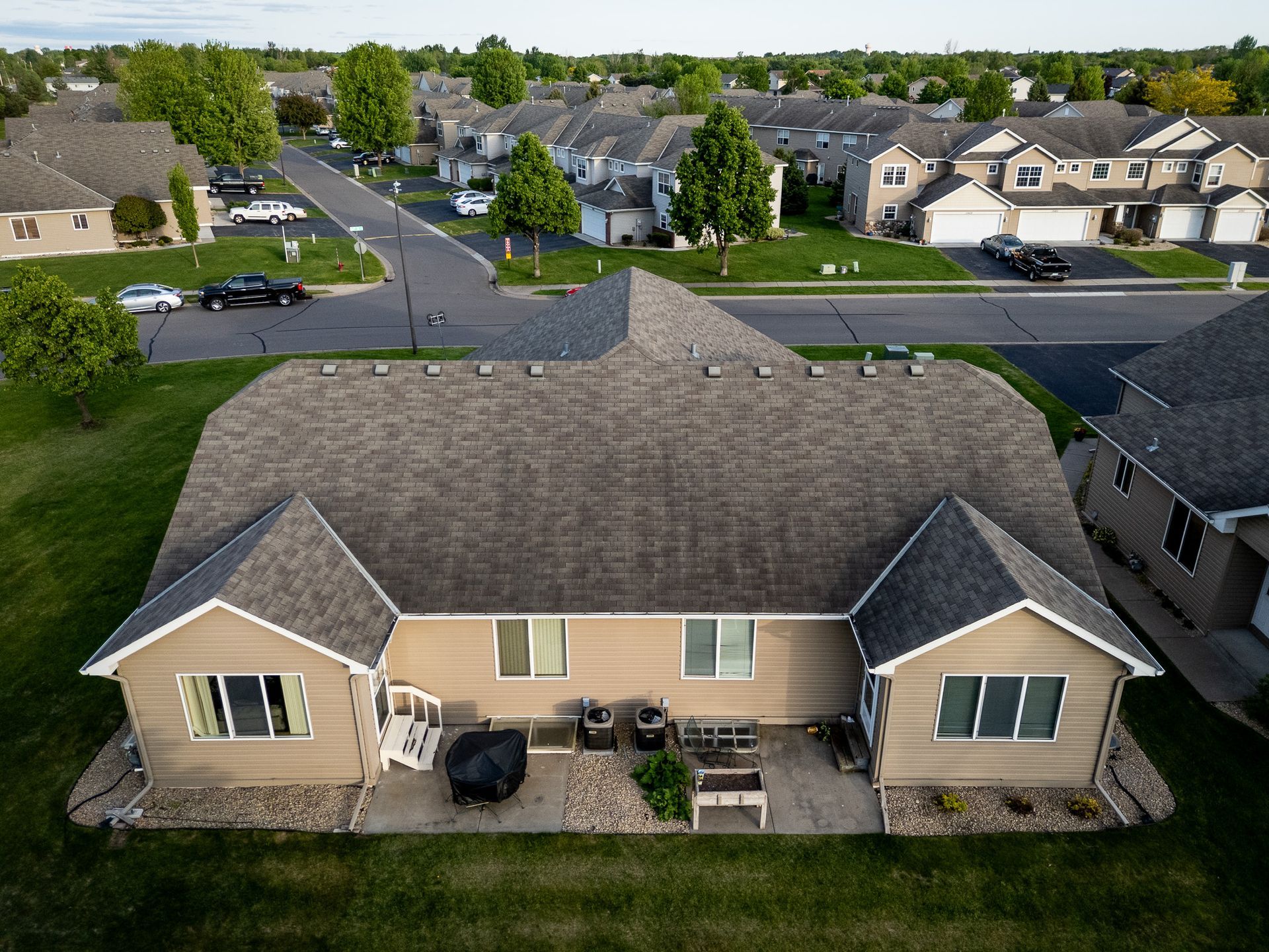 Aerial view of a suburban townhouse with beige siding and gray roof in a residential neighborhood.