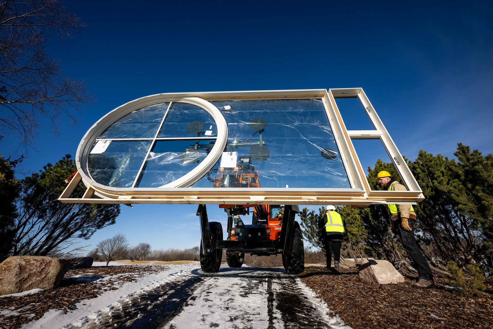 Workers installing a large glass solar panel frame on a road construction site under a blue sky