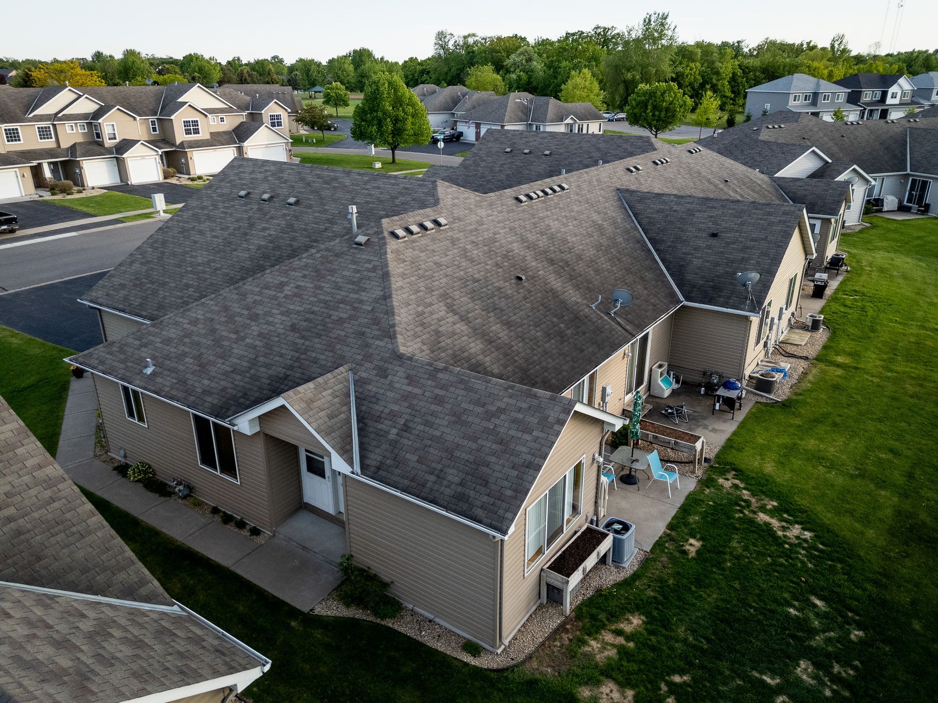 Aerial view of suburban houses with gray roofs and a backyard patio on a grassy lot.