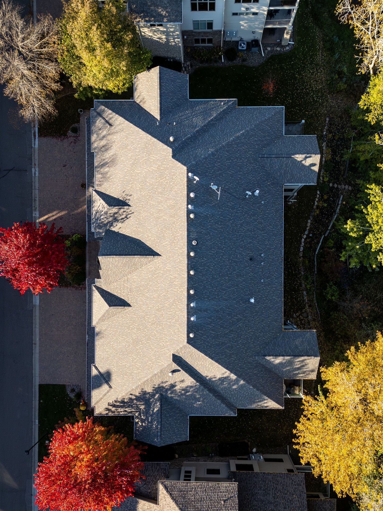 Aerial view of a house with a gray roof, bordered by red and yellow autumn trees.