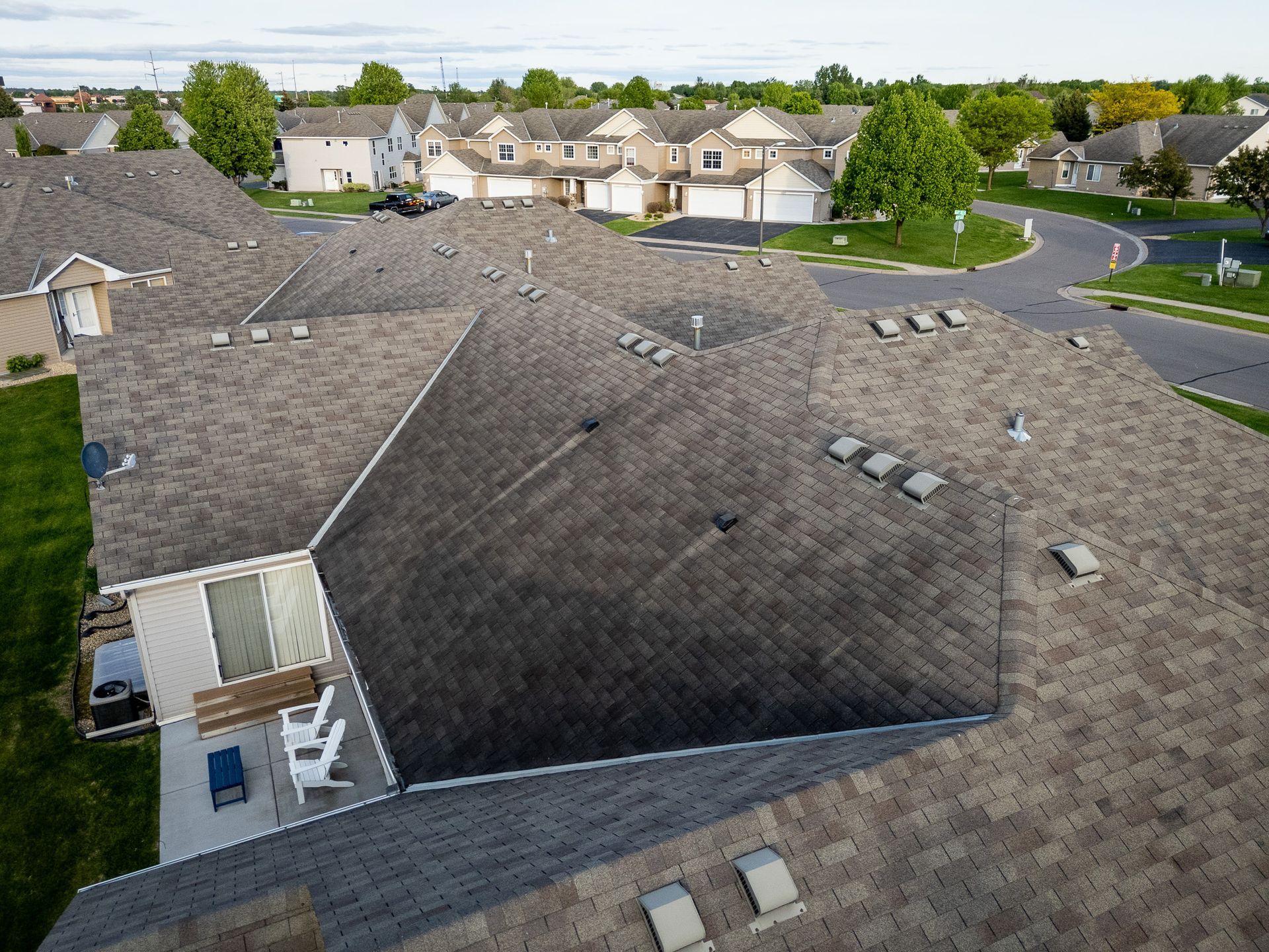 Rooftop view of gray shingle houses in a suburban neighborhood, with trees and streets in the background