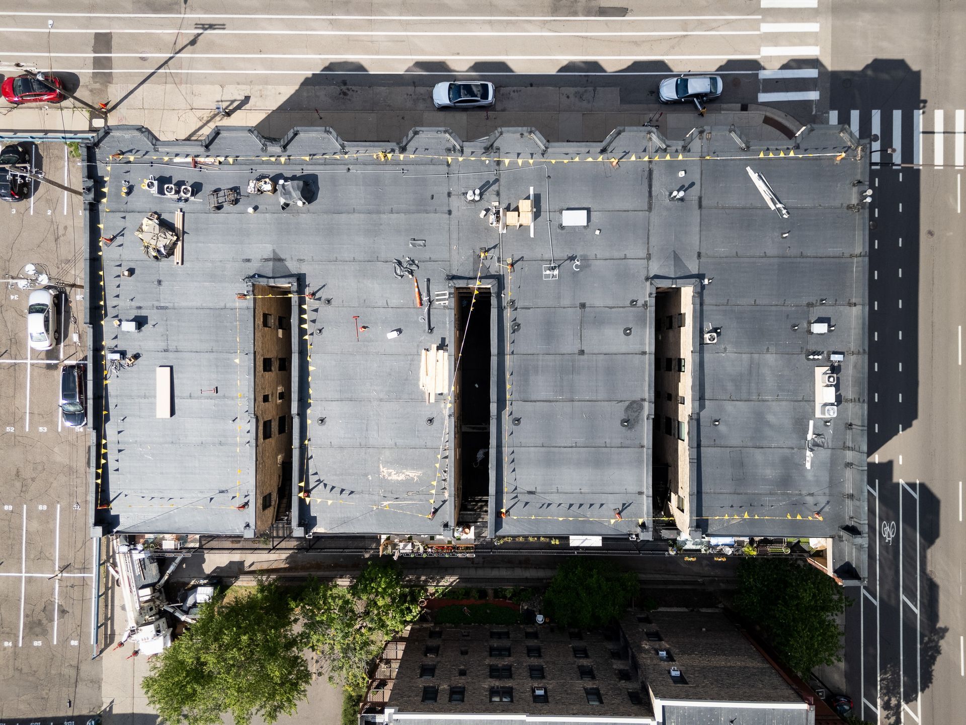 Aerial view of a flat rooftop with vents and skylights beside a street and parked cars