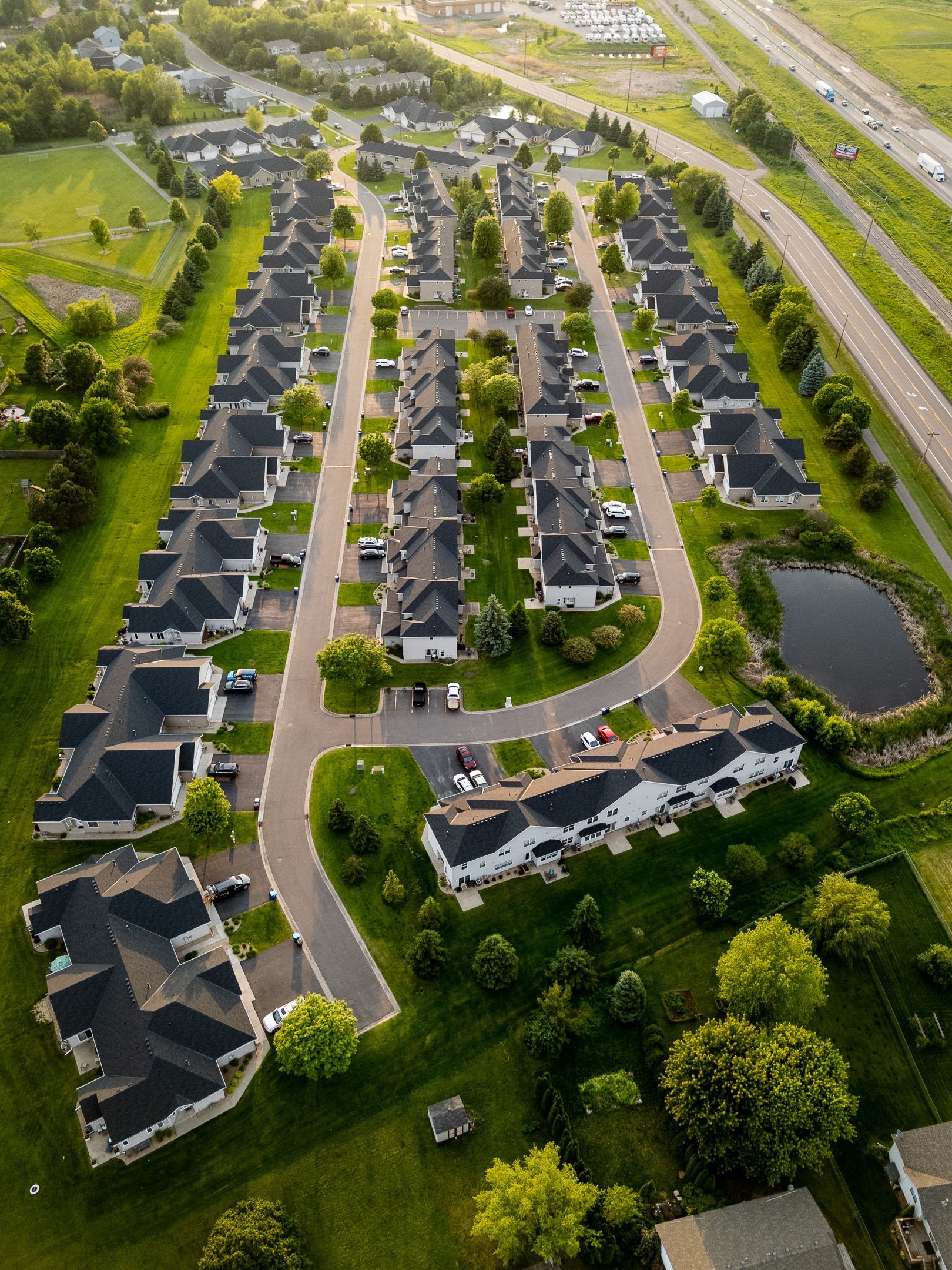 Aerial view of a suburban neighborhood with rows of houses, roads, and green lawns near a highway